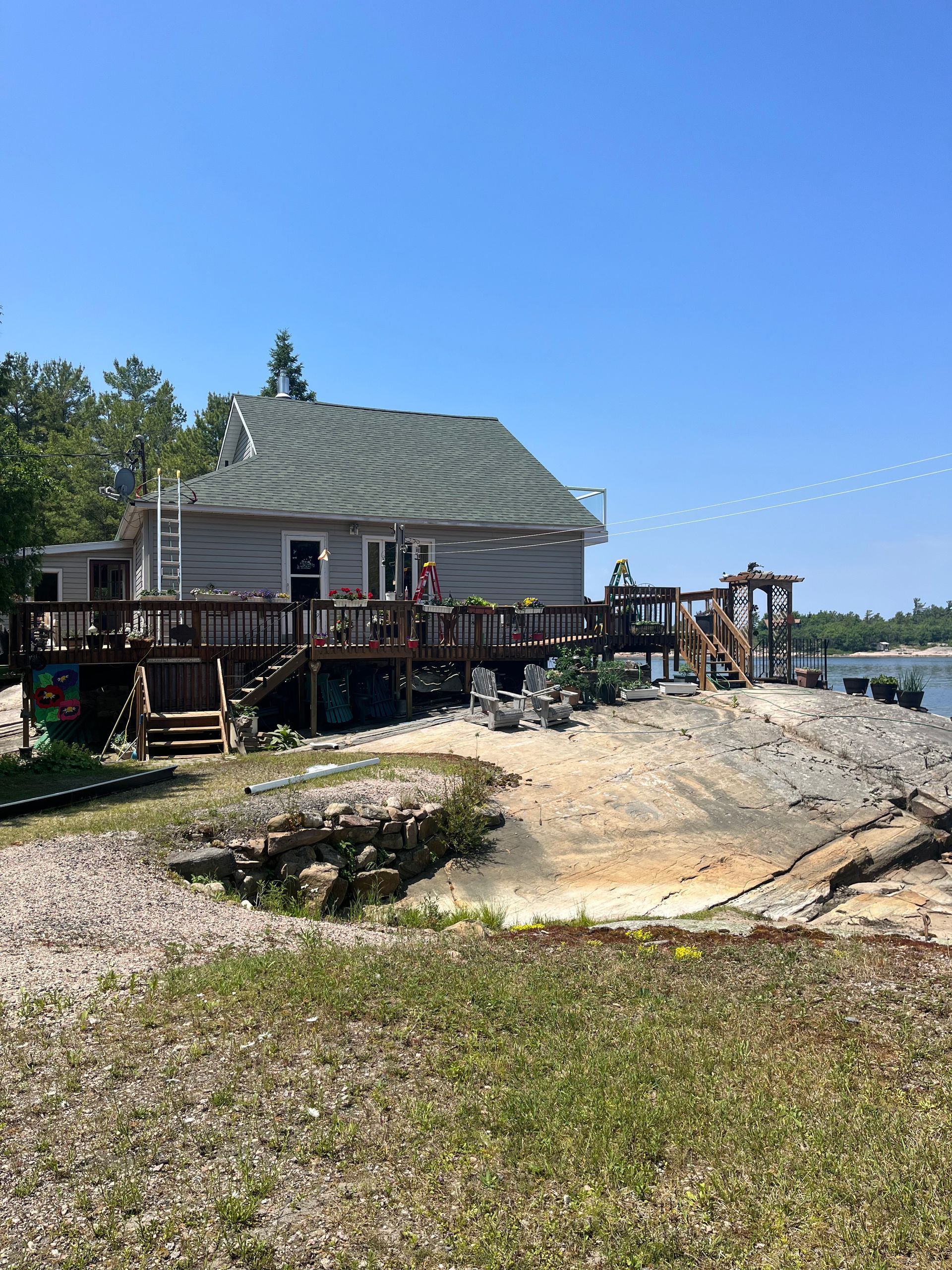 Weathered seaside cottage with a wooden deck on rocky shore under a clear blue sky