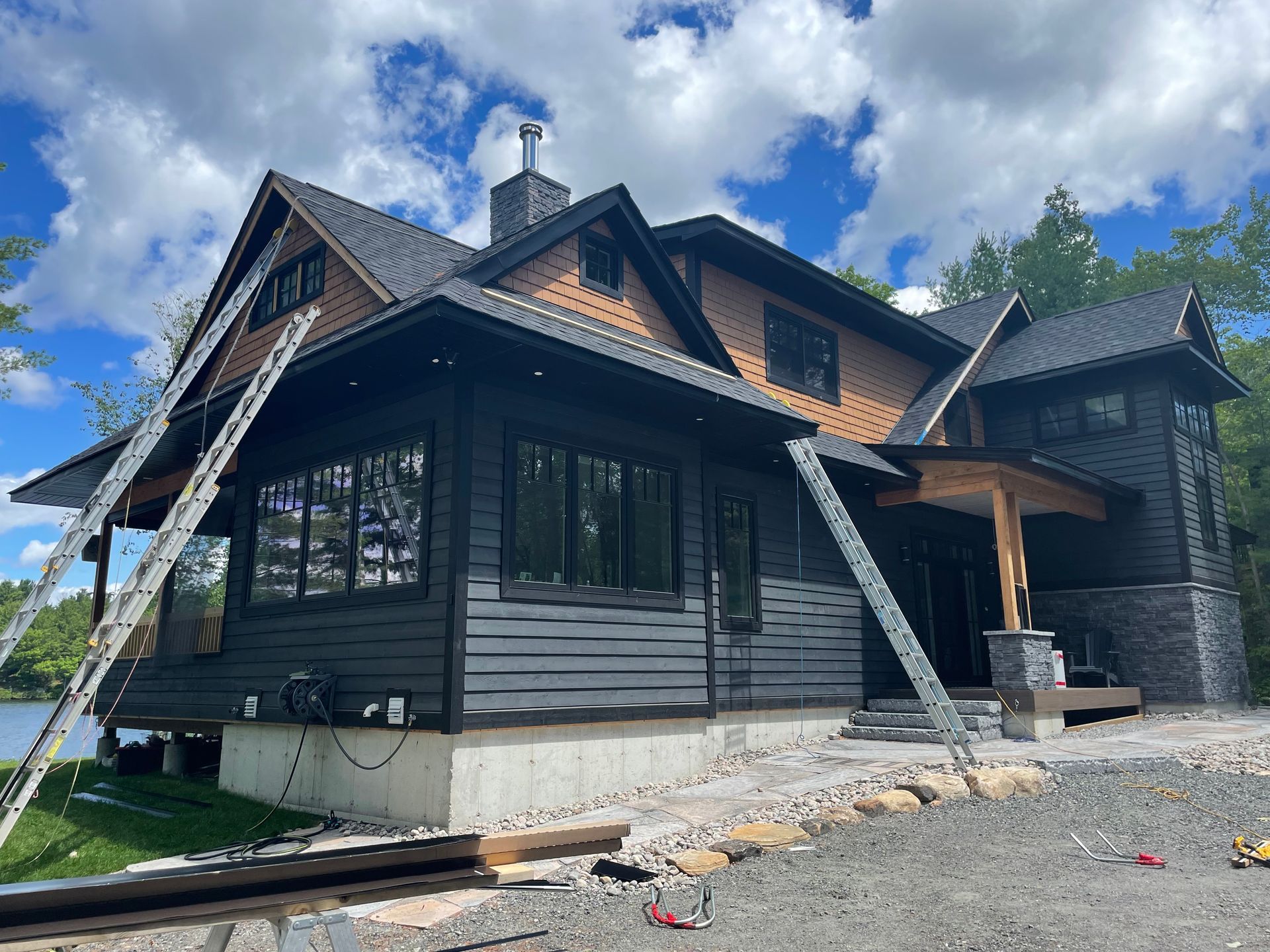 Dark gray house under construction with ladders leaning against the roof and porch.