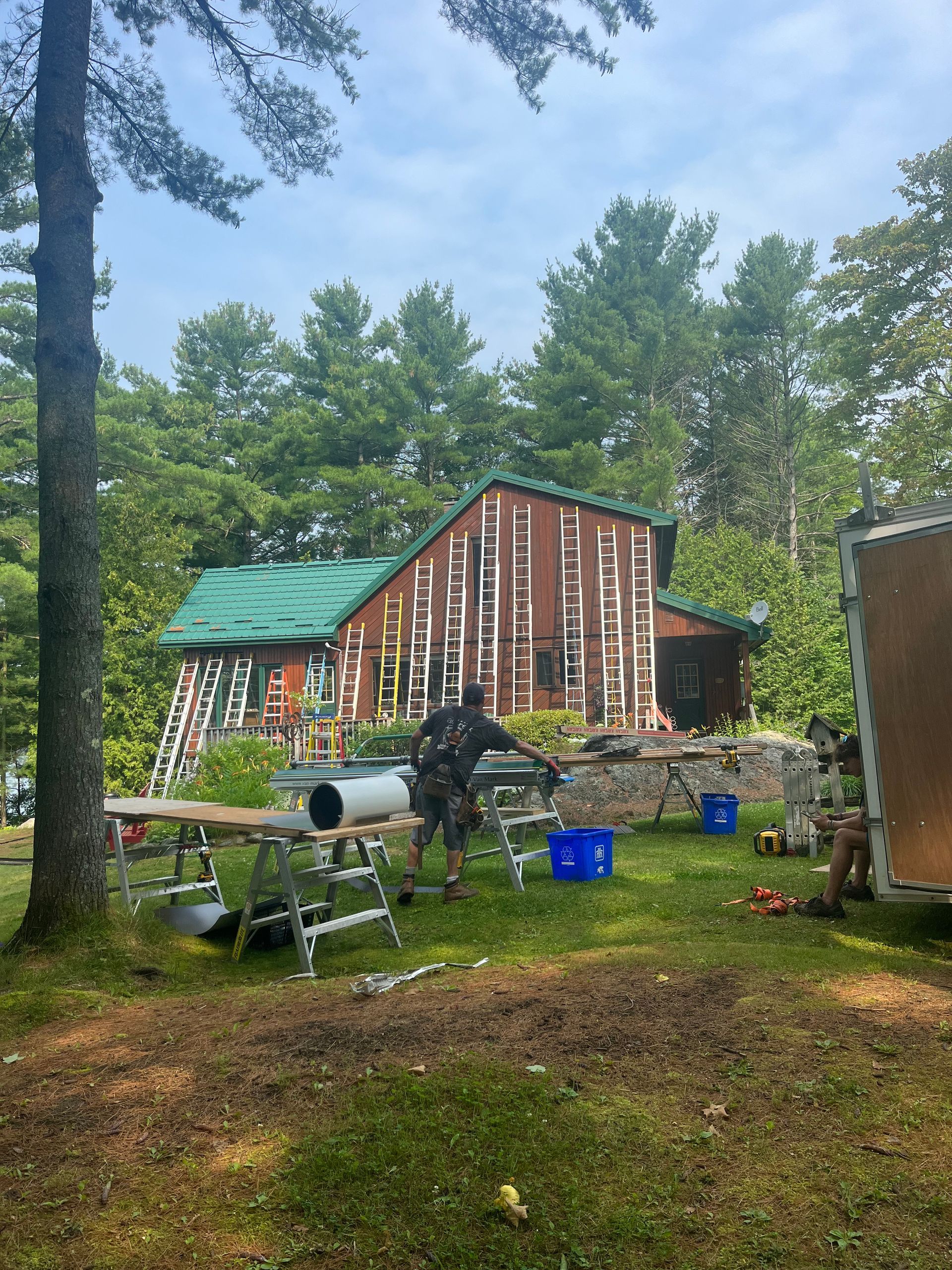 Wooded yard with a rustic red cabin, green roof, and lawn chairs among trees