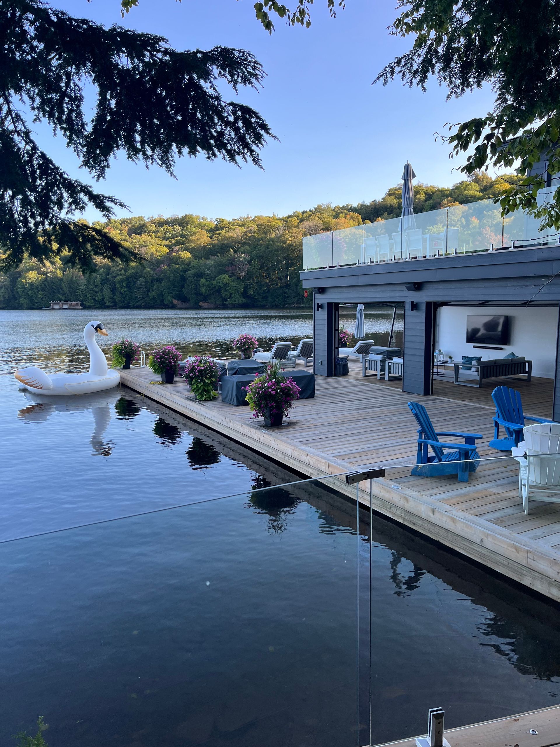 Lakeside patio with blue chairs, potted flowers, and a dock beside calm water at sunset