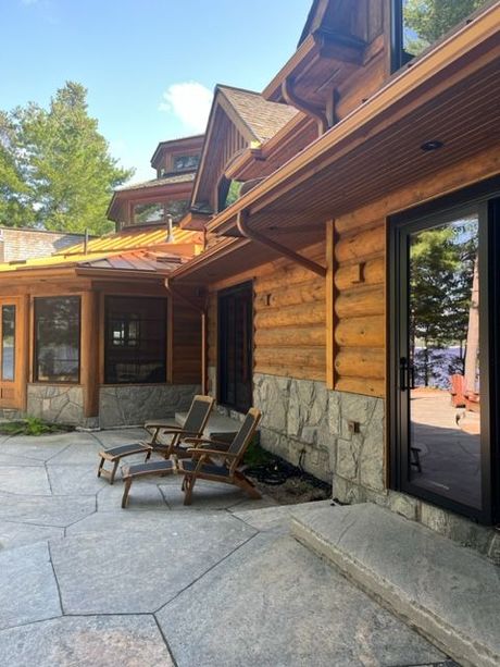 Log cabin lodge patio with stone paving, lounge chairs, and glass doors under a wooden eave
