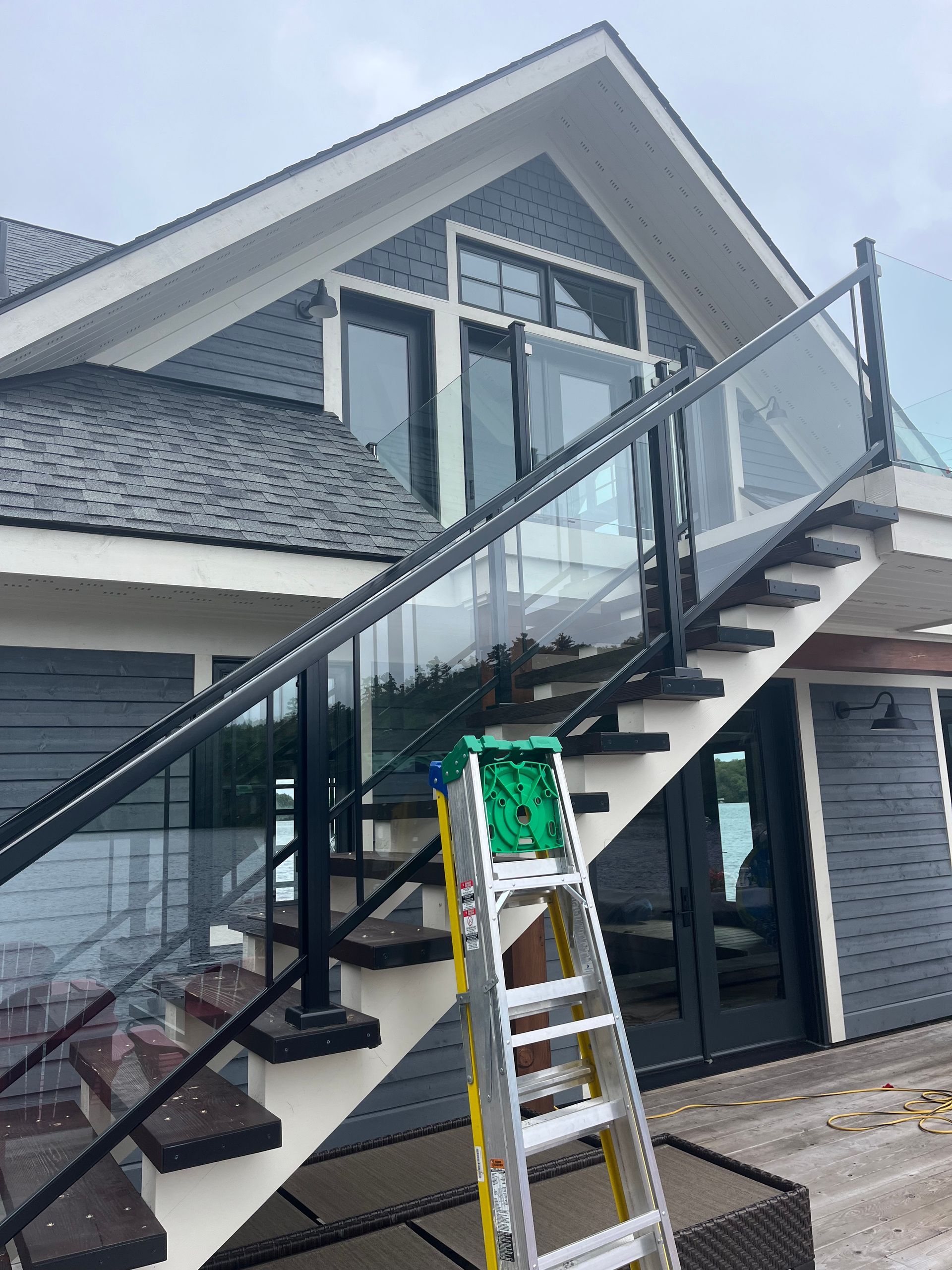 Exterior staircase with glass railing and a ladder beside a gray house under construction