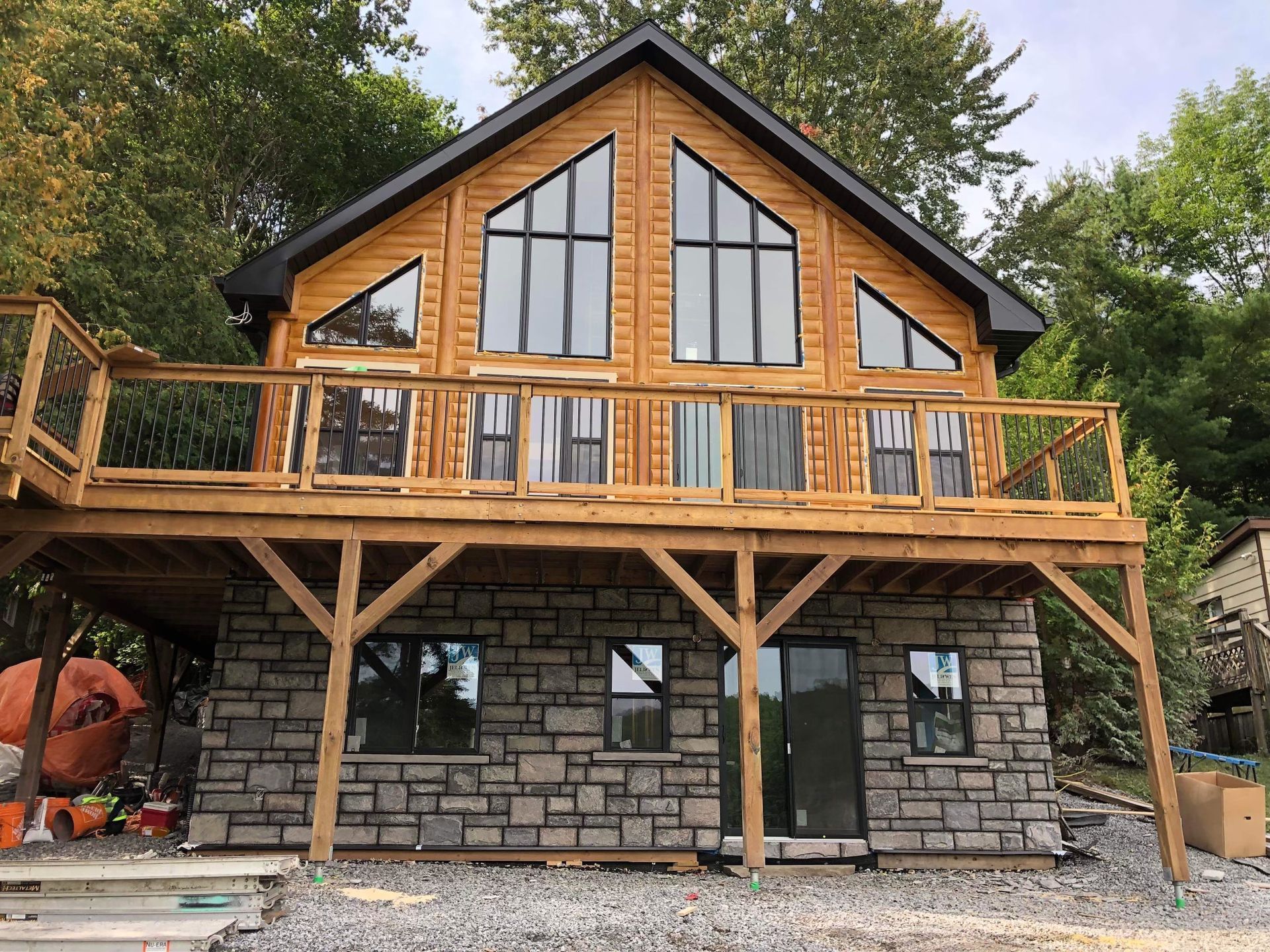 Two-story cabin with stone lower level, wood upper level, and wraparound deck in a wooded setting