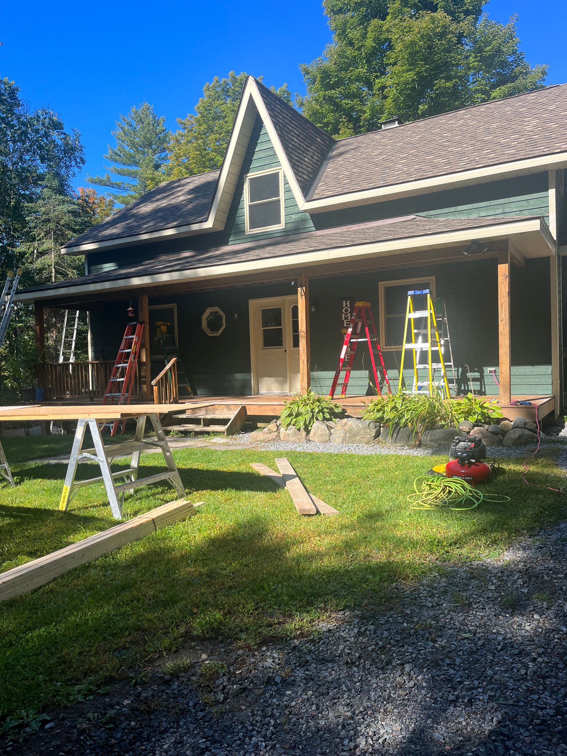 House exterior with porch, ladders, and sawhorses in a sunny yard