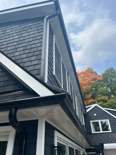 Dark gray-shingled house exterior with white trim and autumn trees in the background