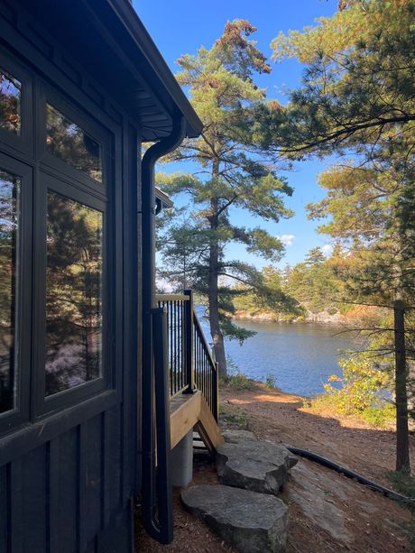 Cabin deck with stone steps overlooking a calm lake under a clear blue sky