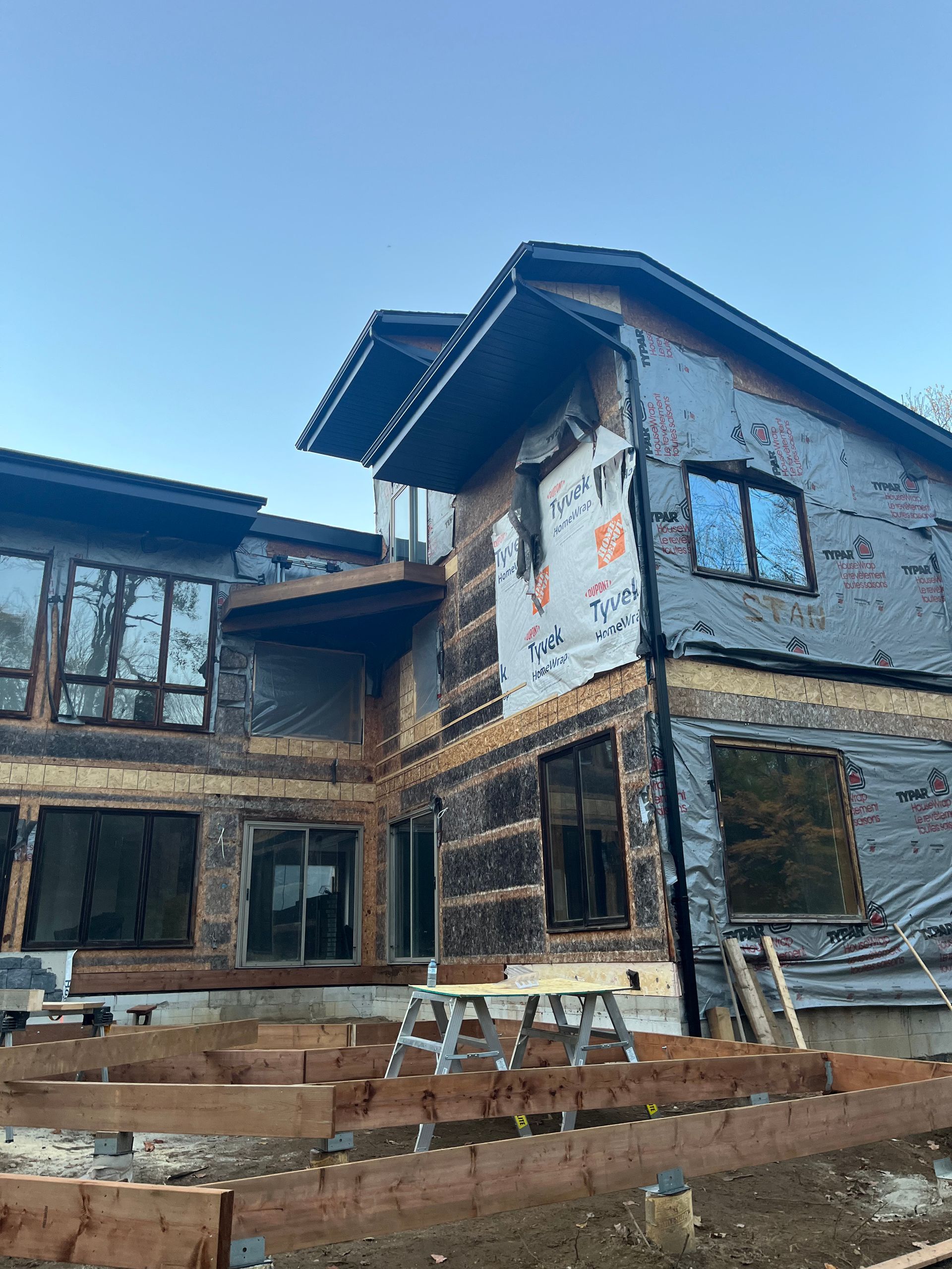 Partially finished house exterior with exposed brick, white stucco, and wooden scaffolding under a blue sky