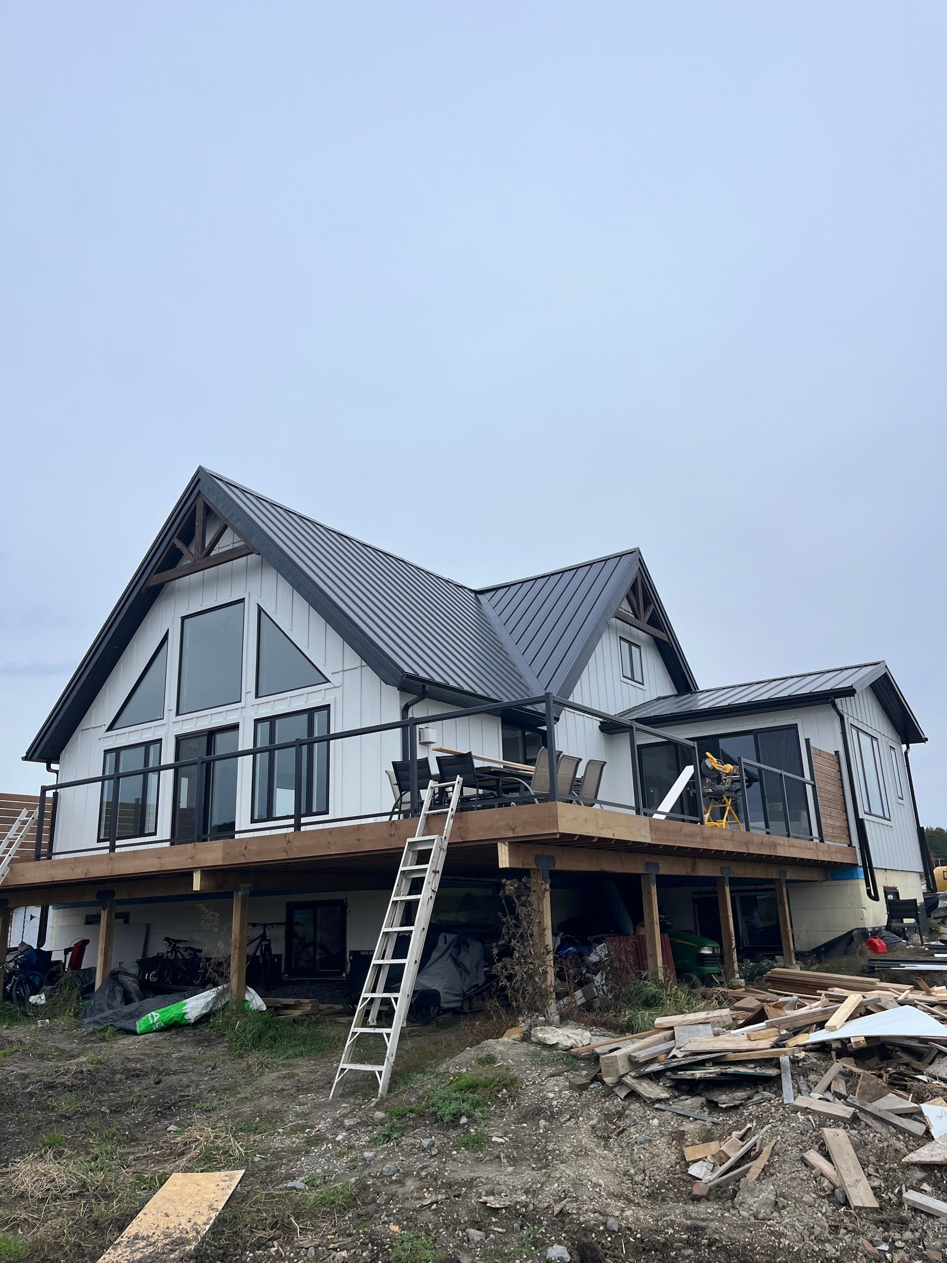 Partially built modern house on stilts with a gray roof and ladder on a muddy construction site