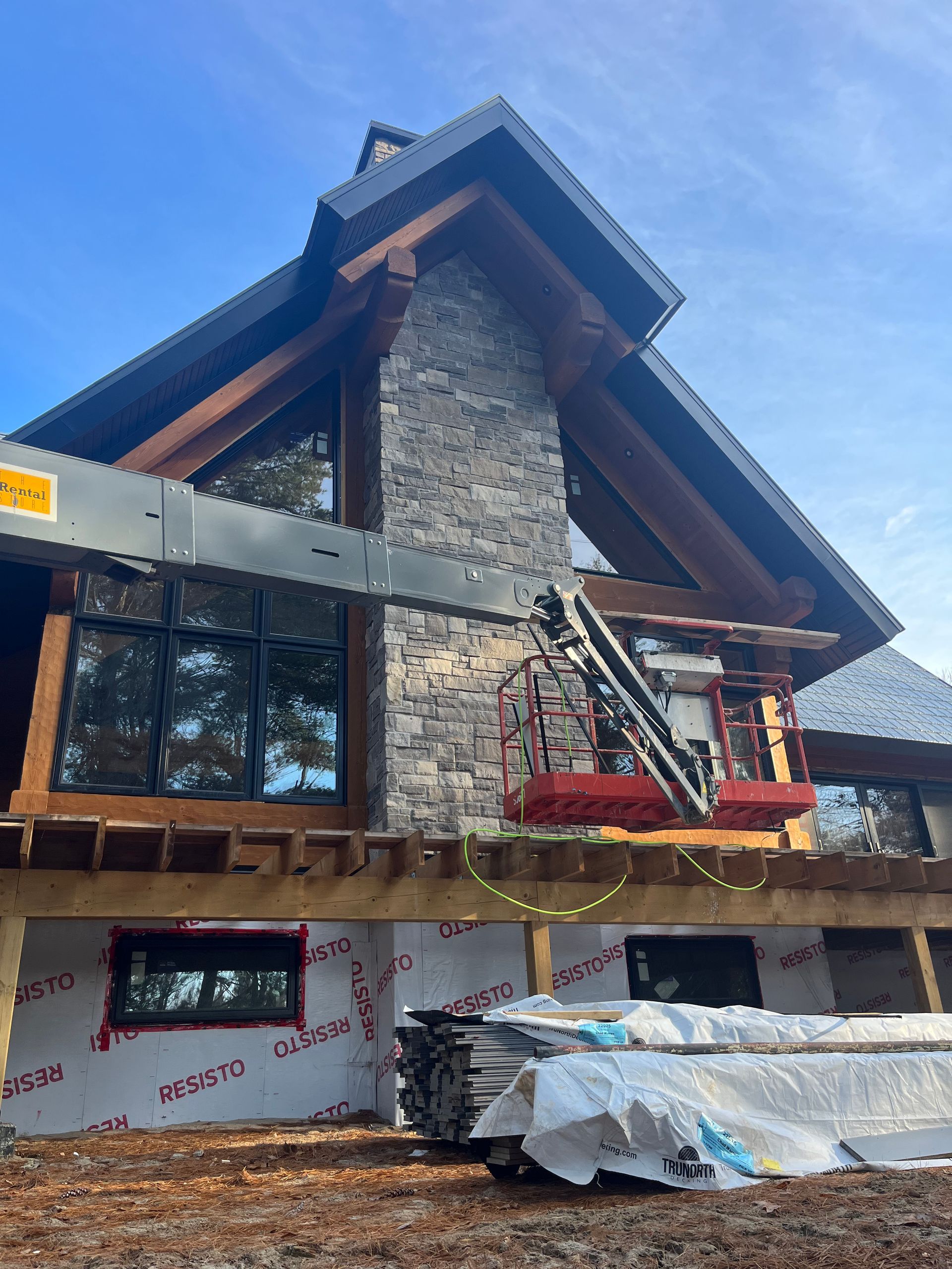 Stone chimney and gabled roof of a house under construction, with scaffolding and covered materials.