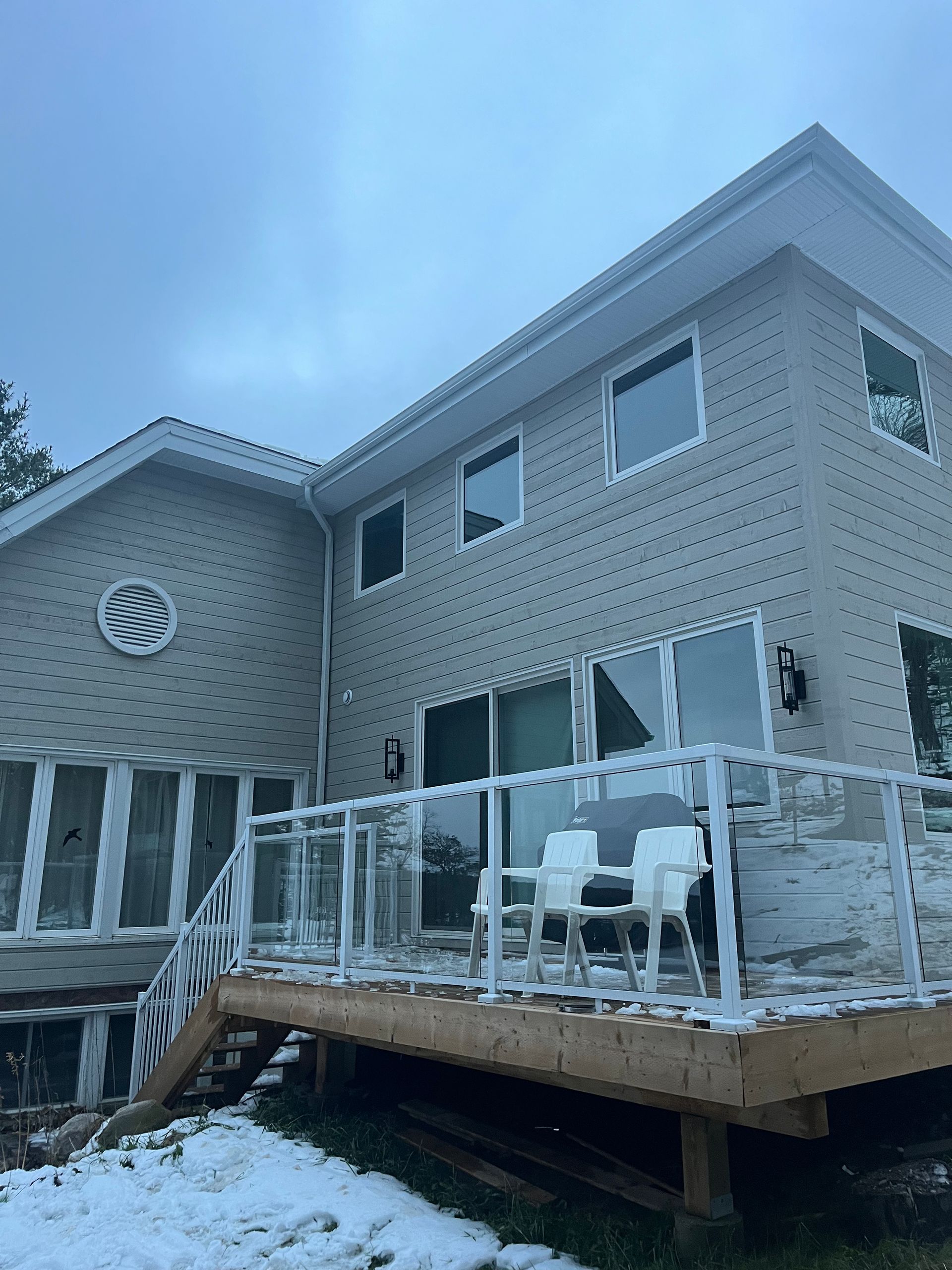 Snowy backyard deck beside a beige house with white railings and outdoor furniture.