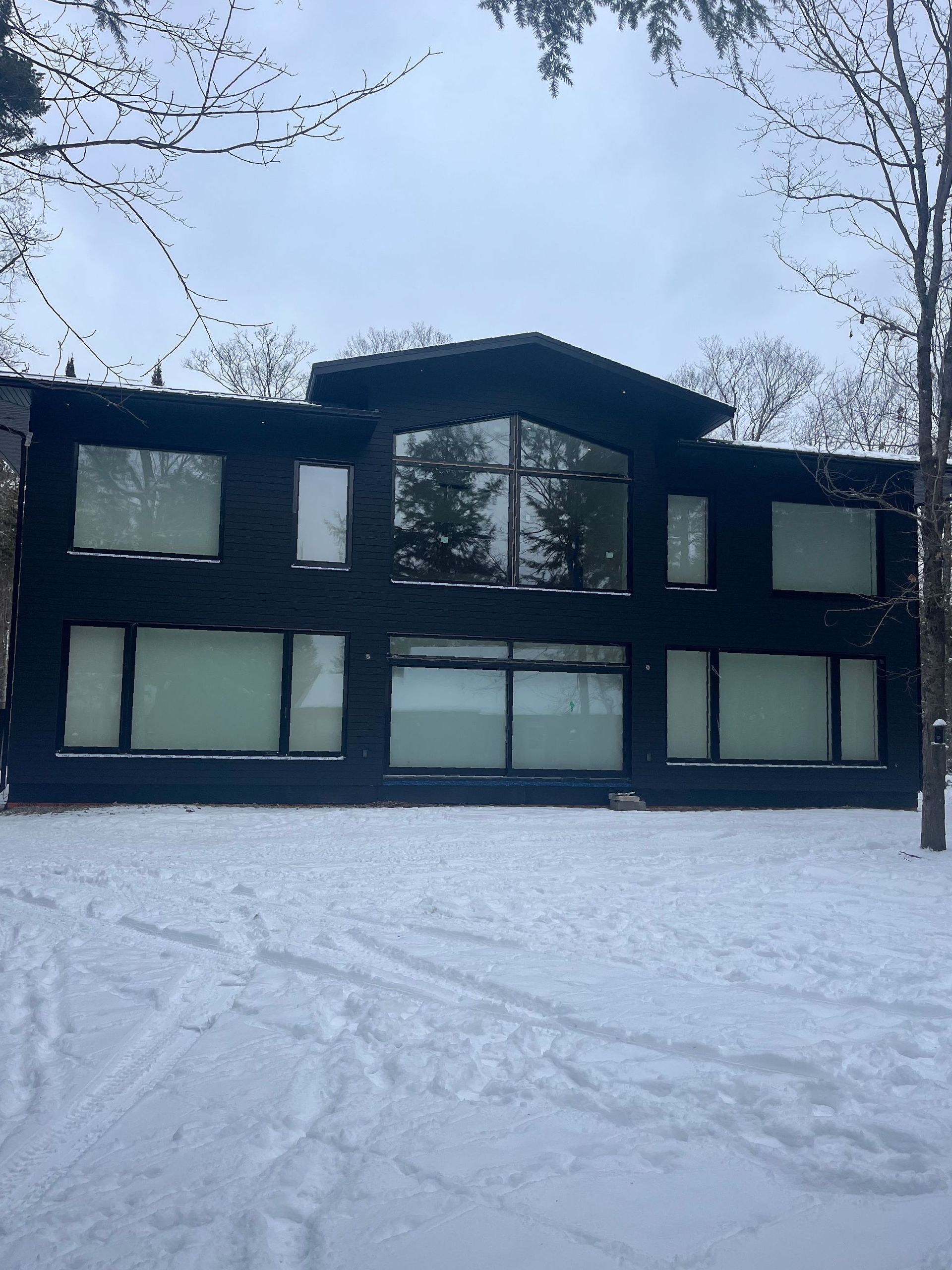 Snow-covered modern black house with large windows and bare trees in winter