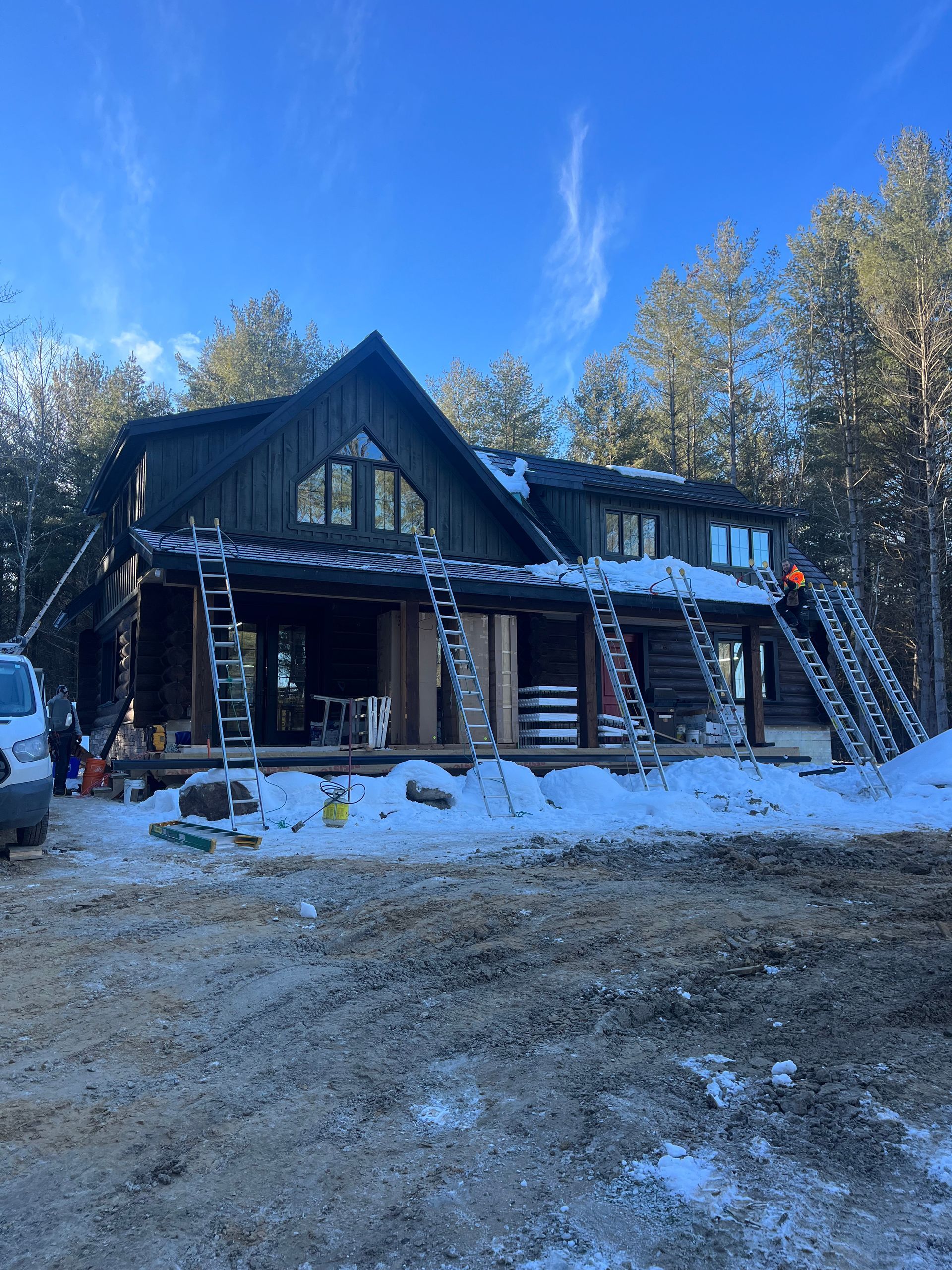 Snowy cabin with a steep roof and striped awning, set in a wooded clearing under a clear blue sky.