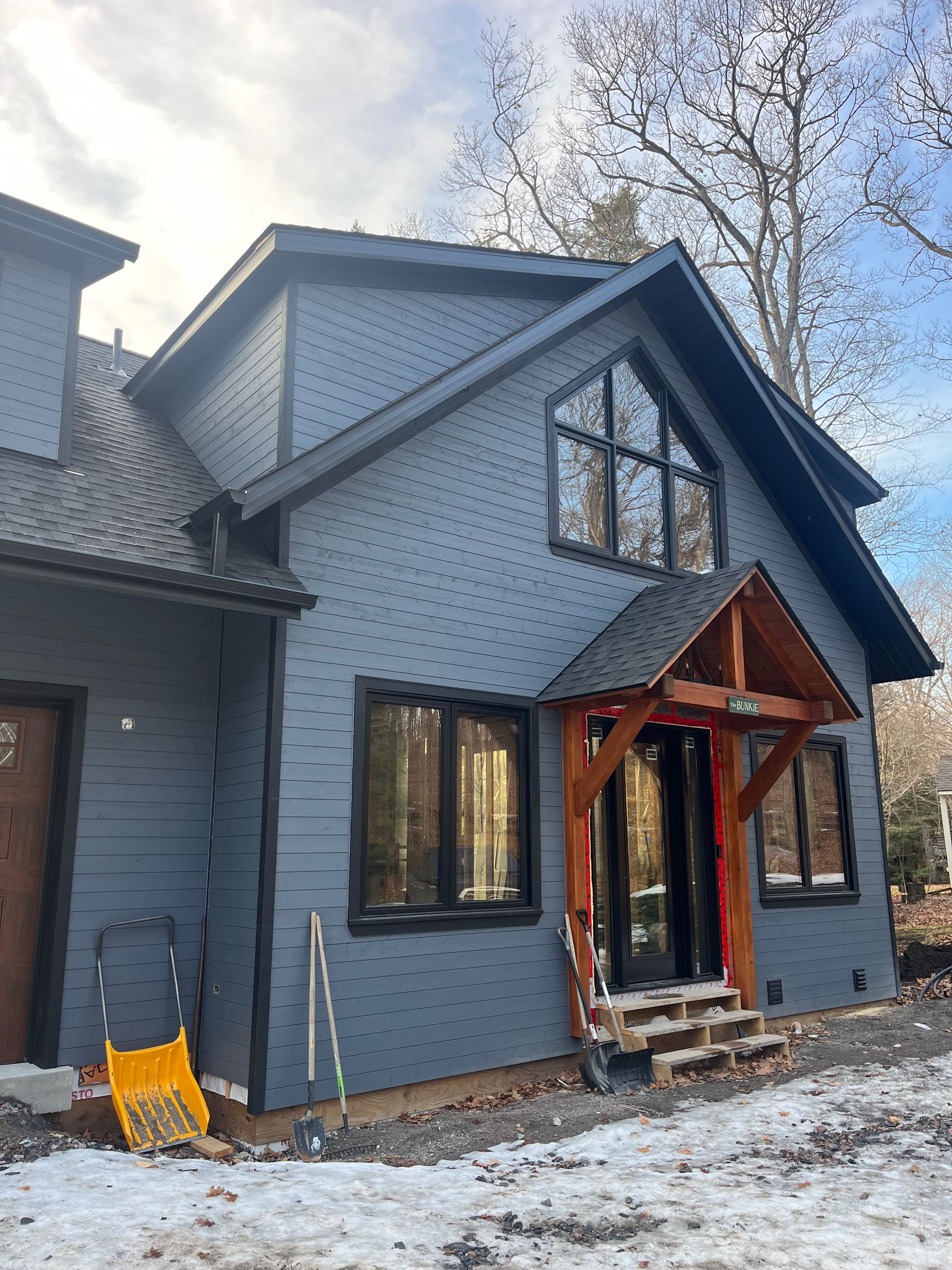 Blue-gray house exterior with a red wooden entry porch in a snowy yard