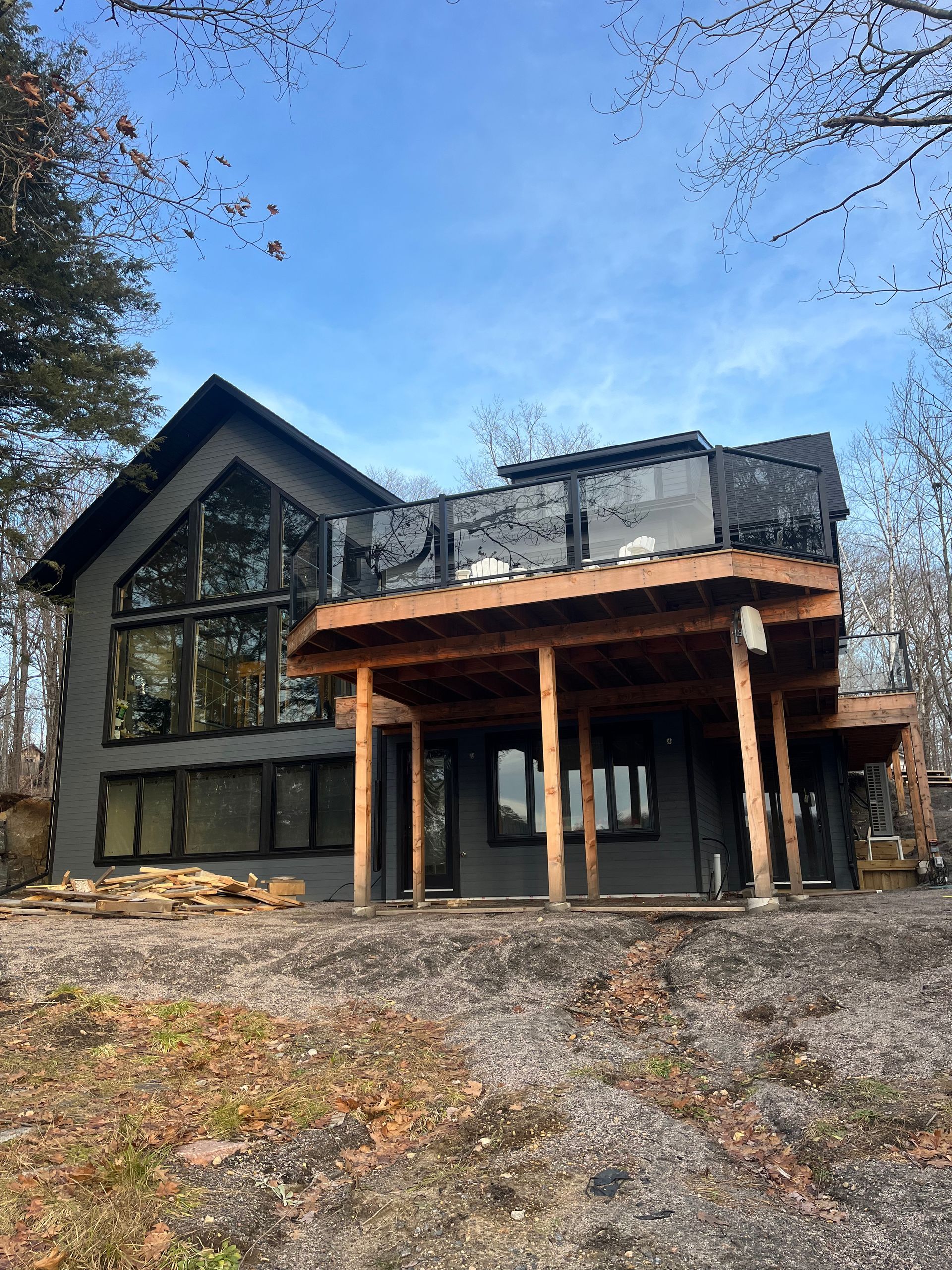 Modern cabin-style house with a stone facade, large windows, and a covered wooden porch in a wooded setting