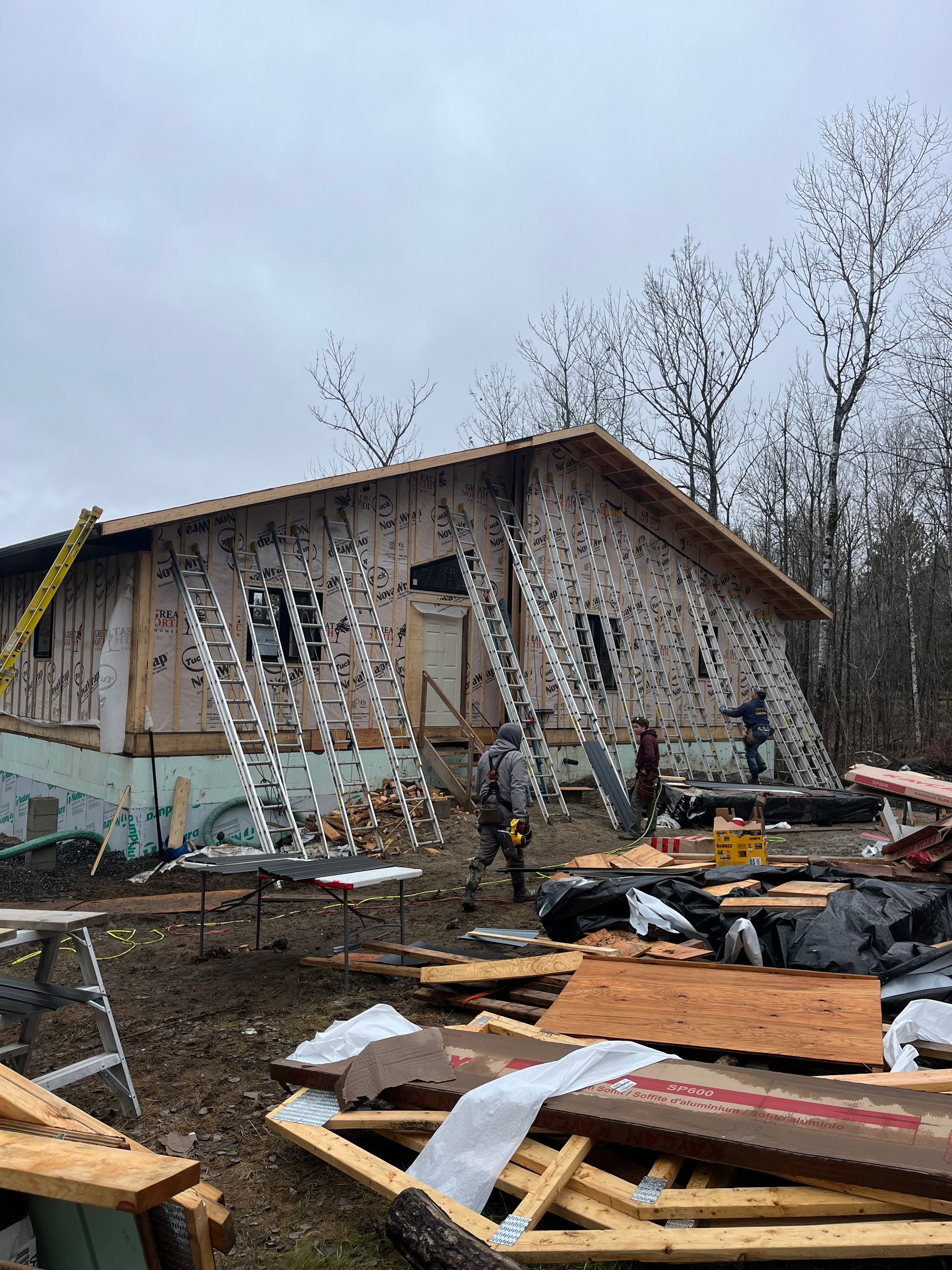 Damaged house under construction with scattered debris and ladders on a muddy lot