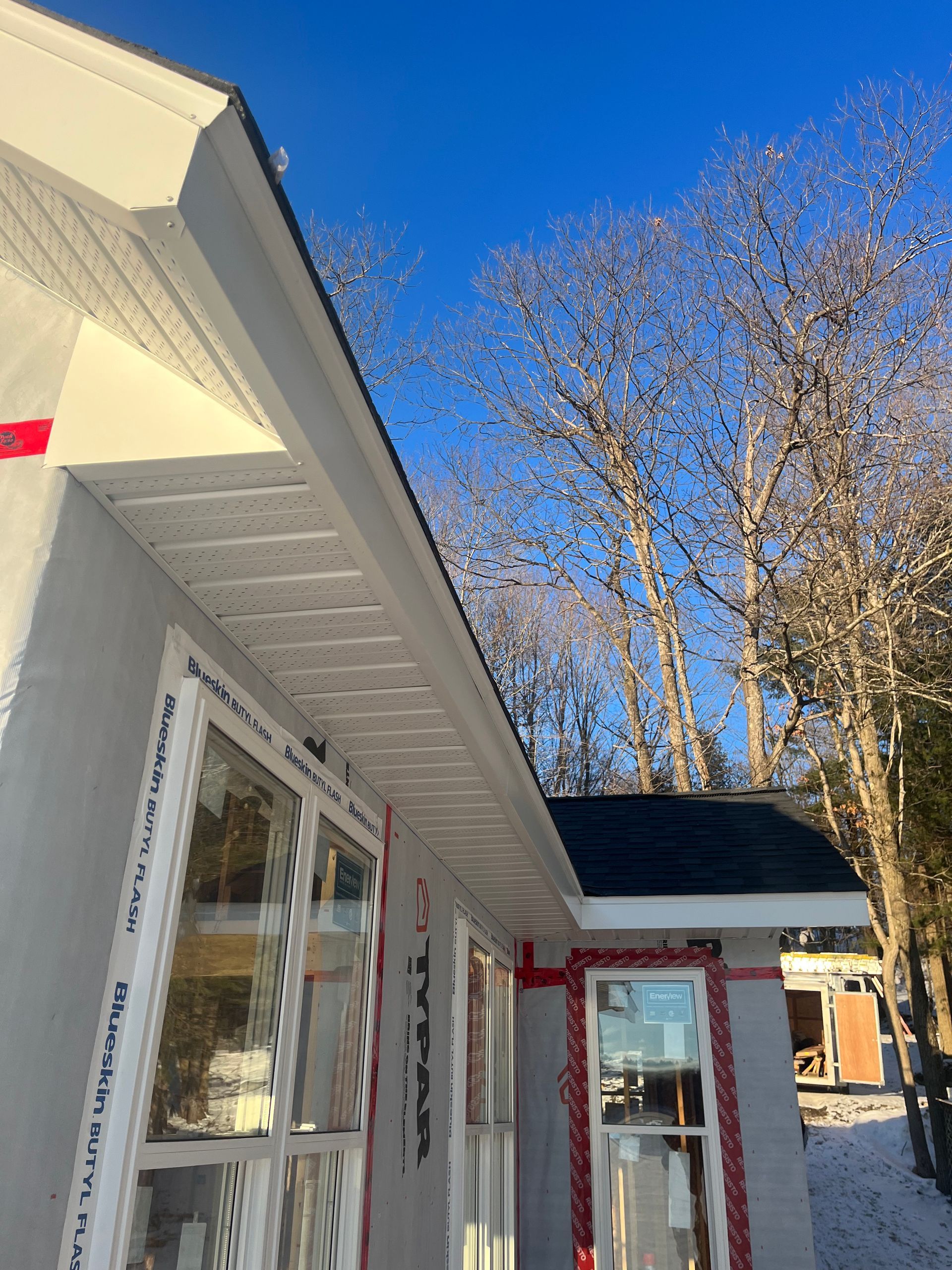 White house exterior with red trim and snow, viewed under a clear blue sky