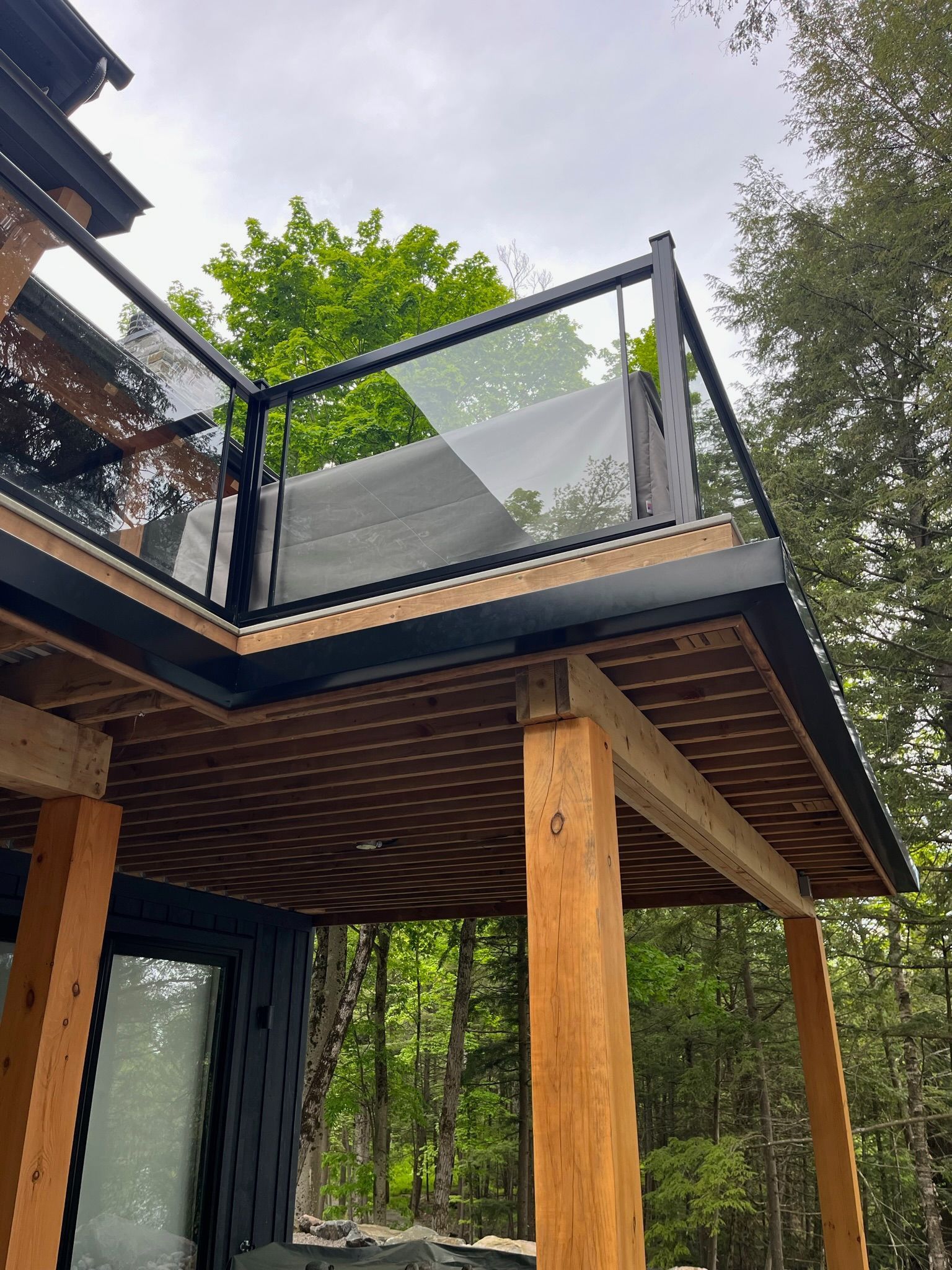 Modern house deck with black railing, wooden posts, and mesh panels overlooking trees