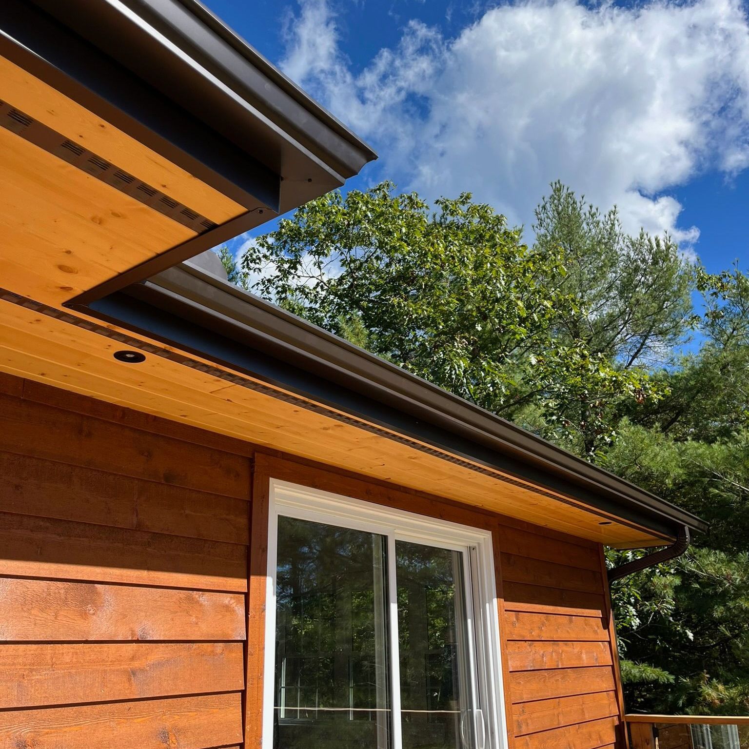 Wooden cabin exterior with a sliding glass door under a blue sky and trees