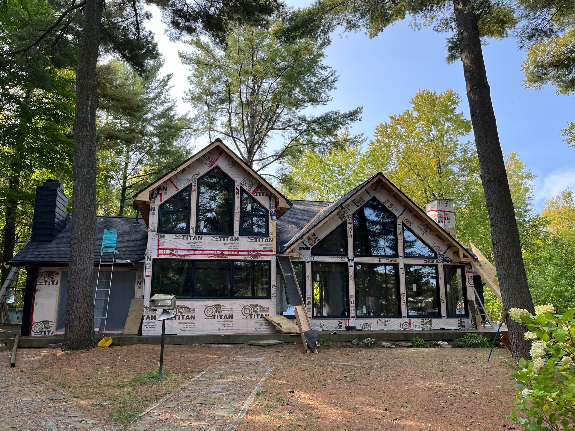 Modern A-frame house with large windows in a wooded setting under tall trees