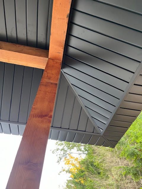 Wooden porch beam and dark gray roof underside with trees visible beyond the edge.