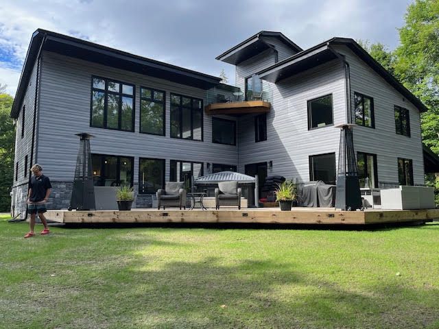 Modern gray two-story house with deck and patio furniture, viewed from a green lawn