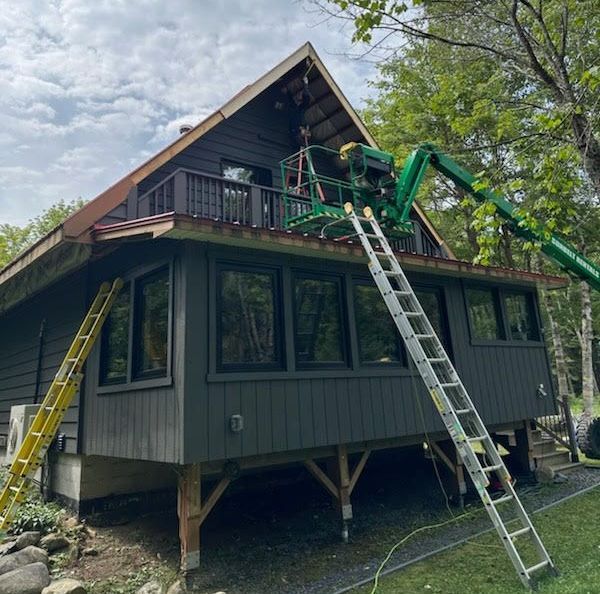 Workers and ladders repairing a gray house with a green lift on the roof.