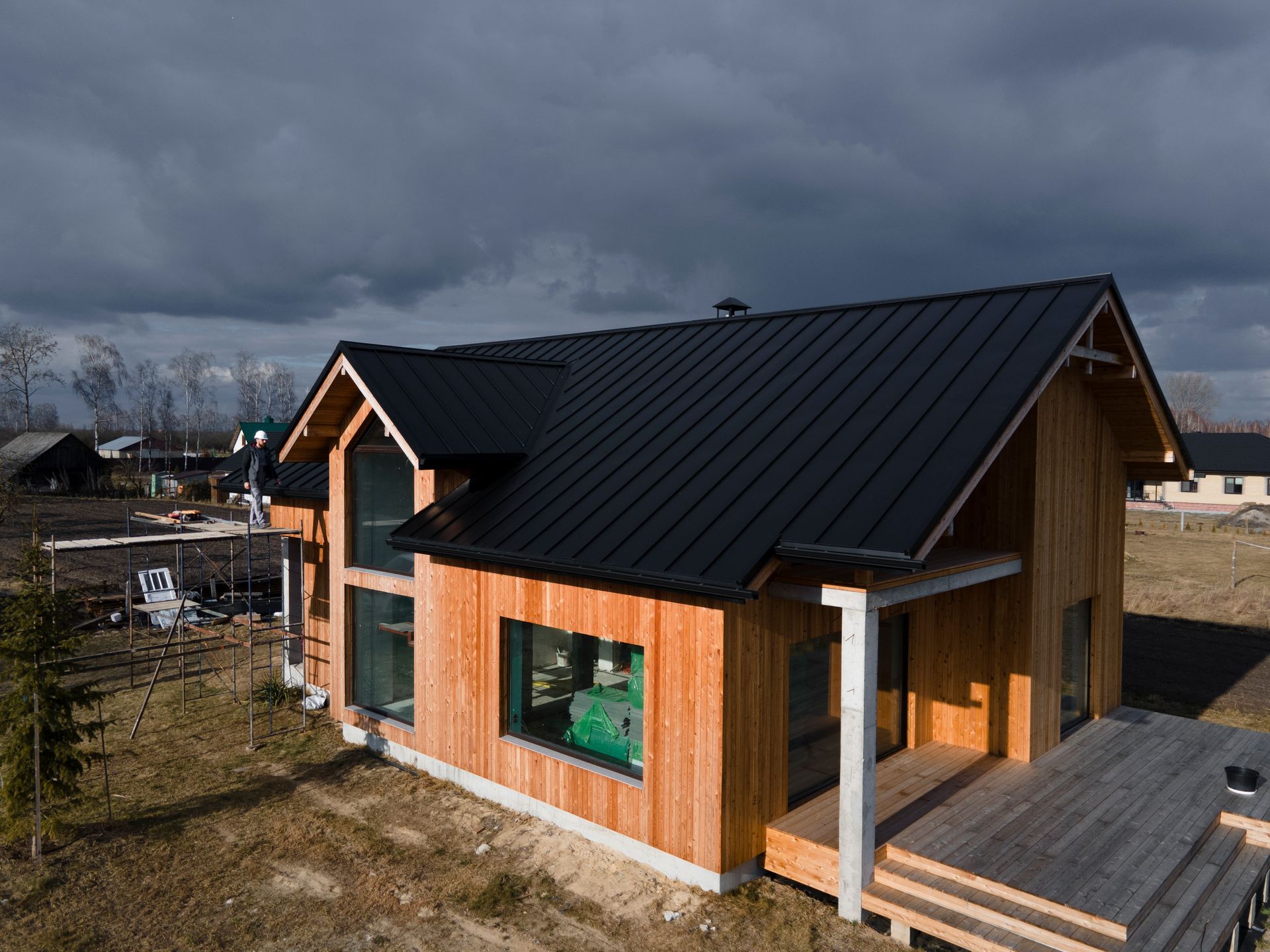 Small modern wooden house with black metal roof and deck under a cloudy sky