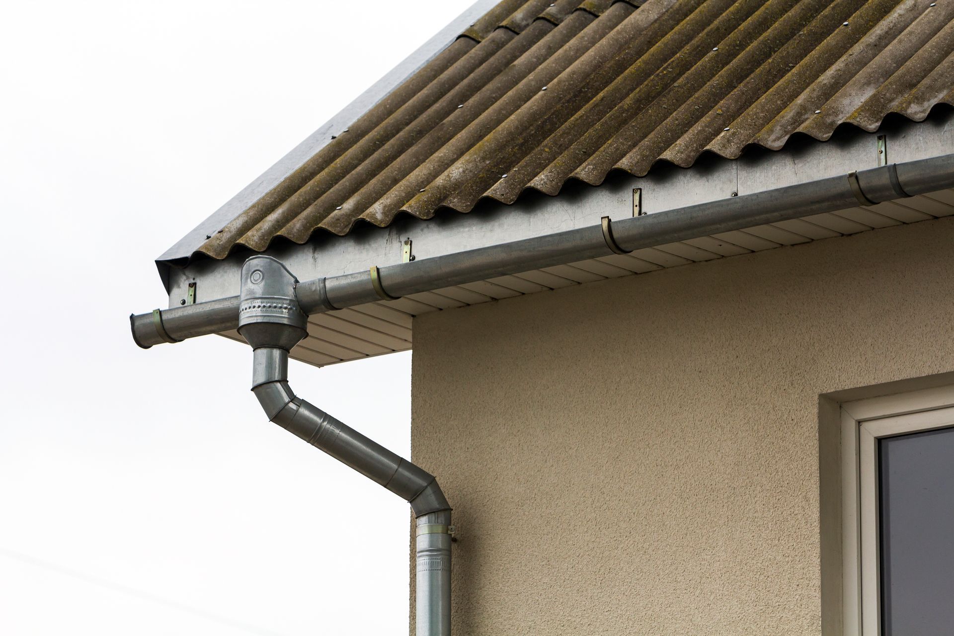 Metal rain gutter and downspout on a beige house under a tiled roof