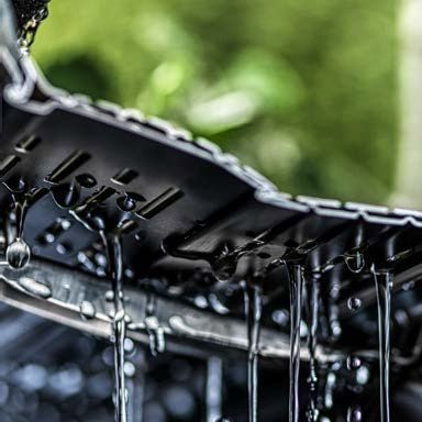 Water streaming off a black car windshield wiper during a wash, with blurred green background
