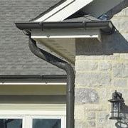 House eaves with a bent black downspout beside a stone wall and window