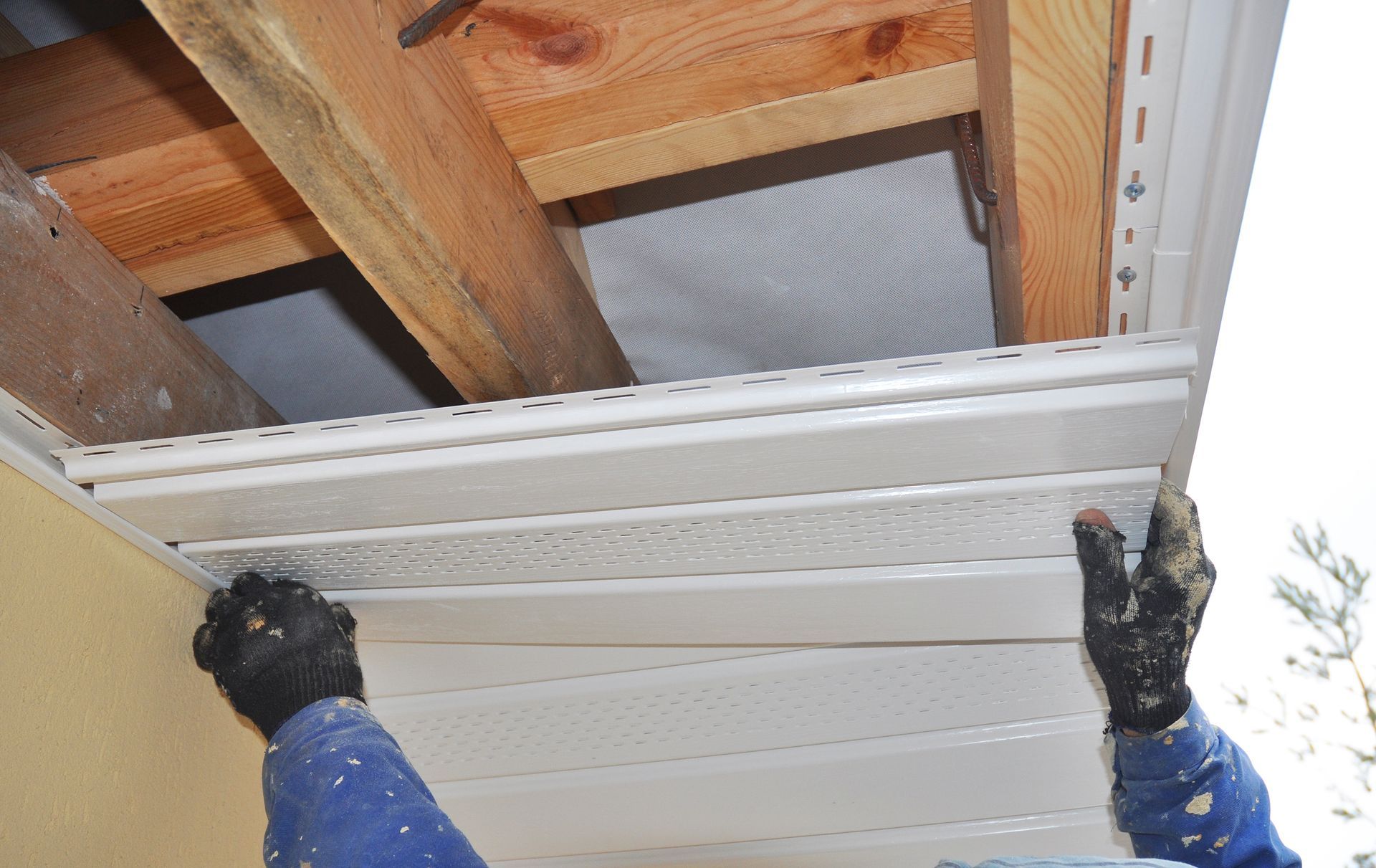Gloved hands lifting a white garage door panel under exposed wooden ceiling beams