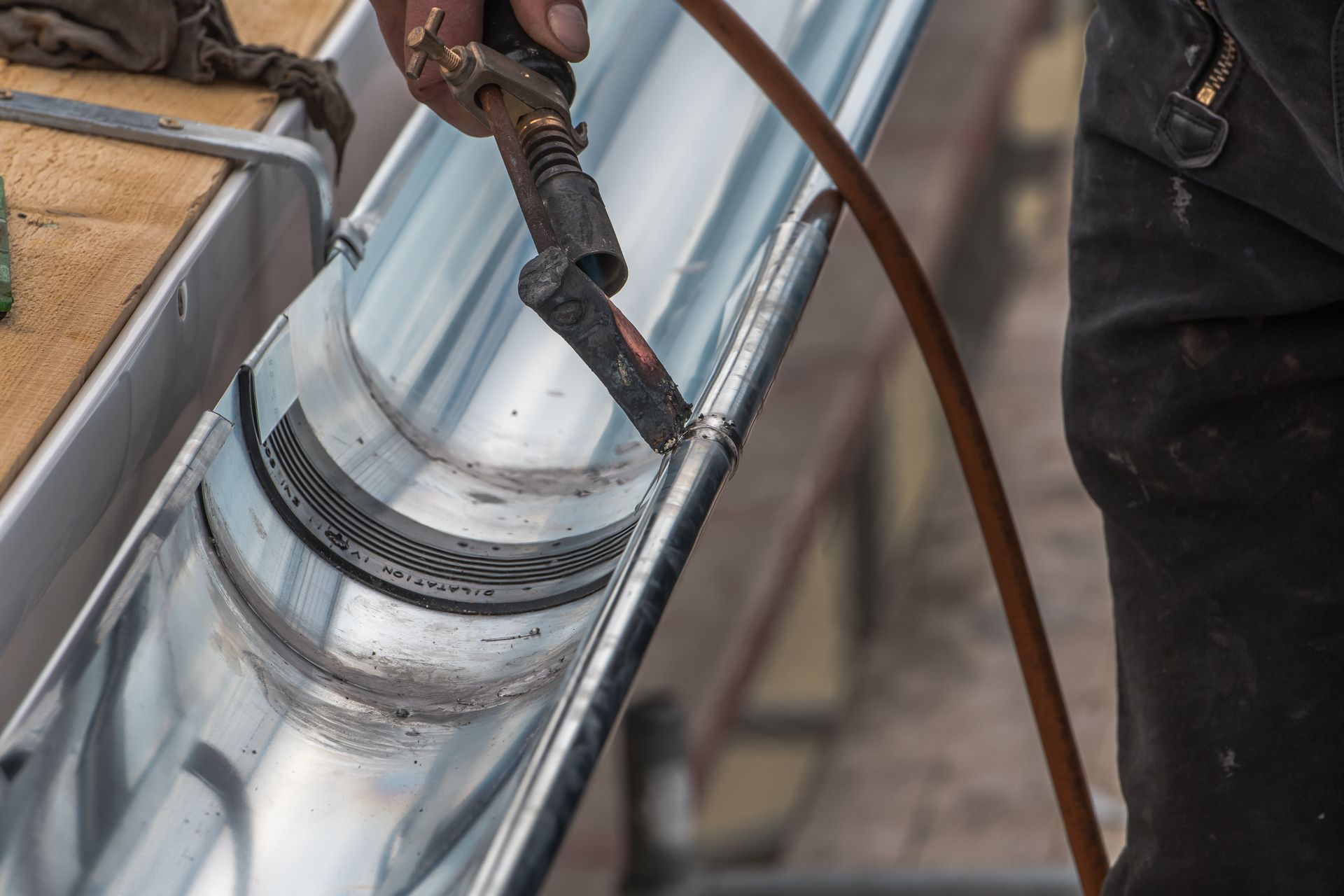 Worker welding a shiny metal pipe with a torch and hose attached