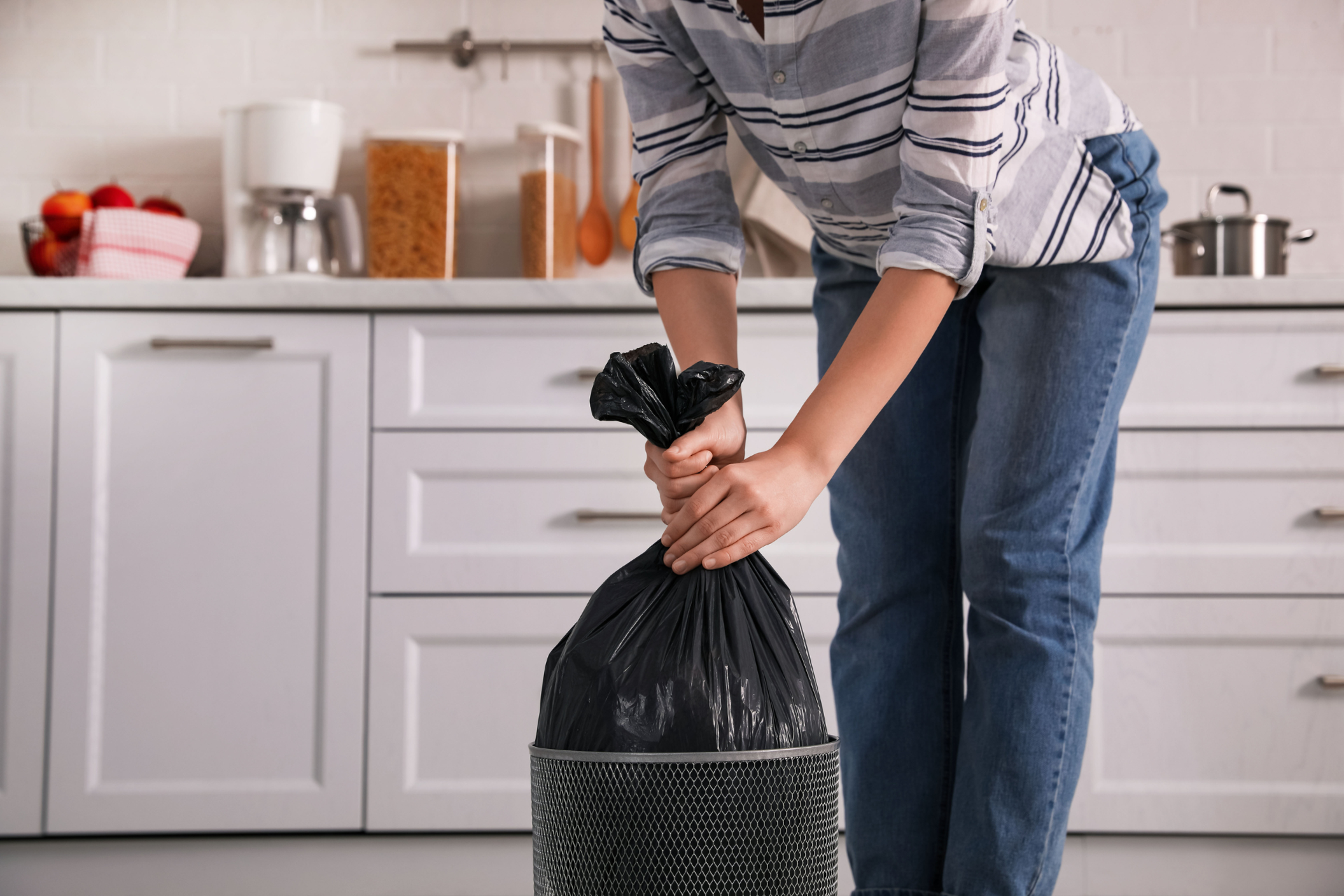 A woman is holding a trash bag in a kitchen.