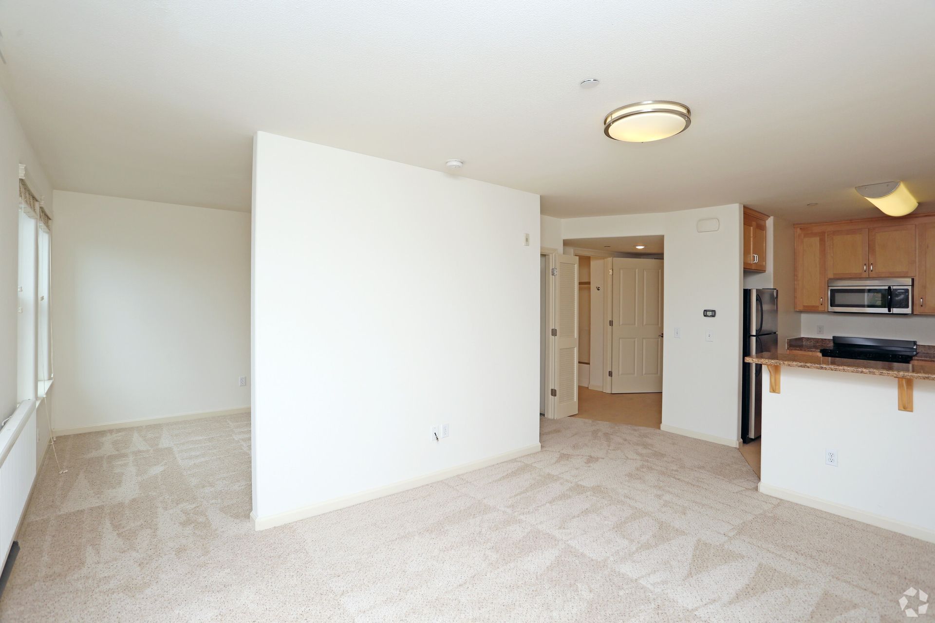 An empty living room with a kitchen in the background