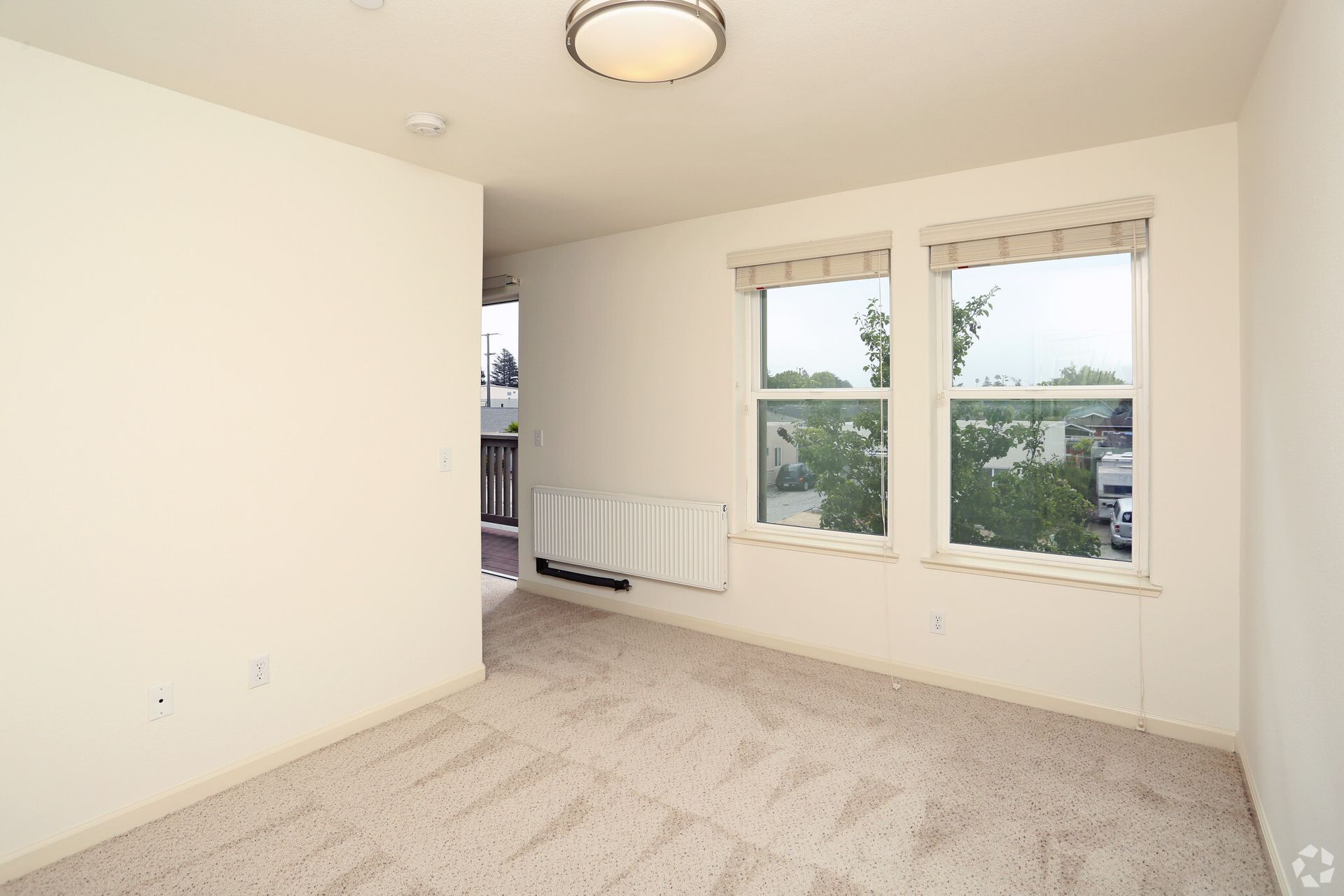 An empty bedroom with two windows and a ceiling light