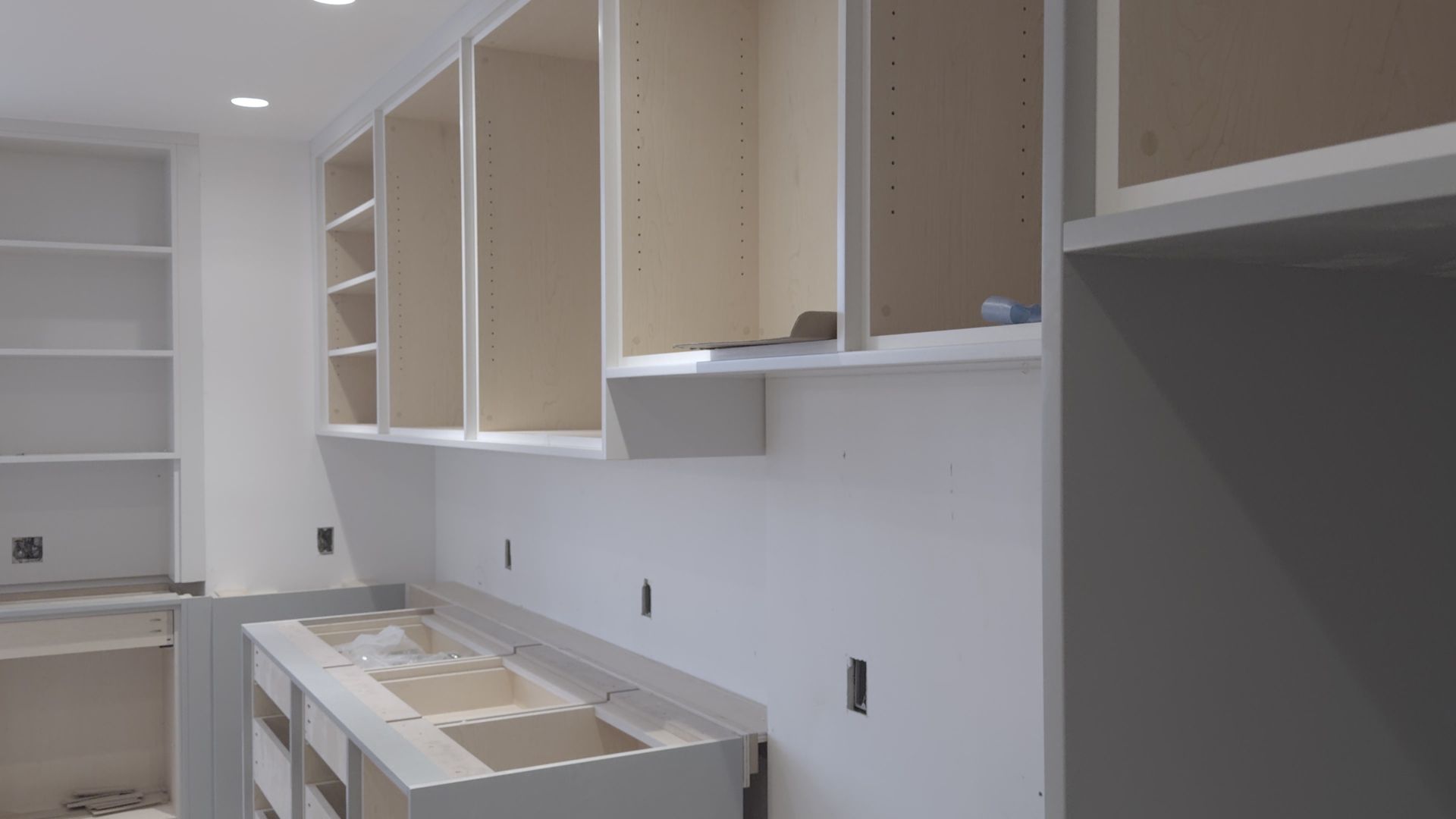 Bright unfinished kitchen with white cabinets, open shelves, and countertops under construction
