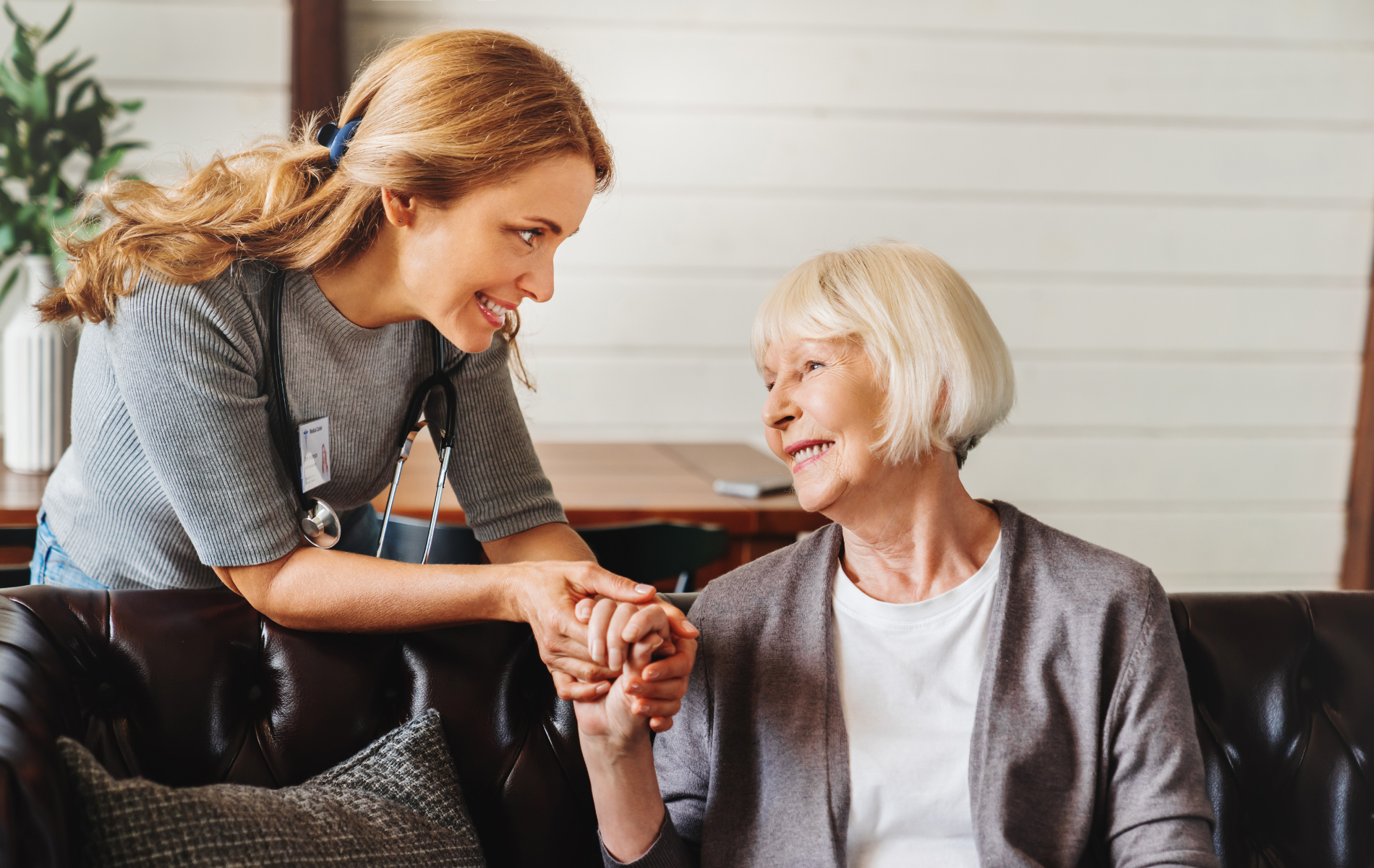 Two women smiling and holding hands on a couch in a bright living room