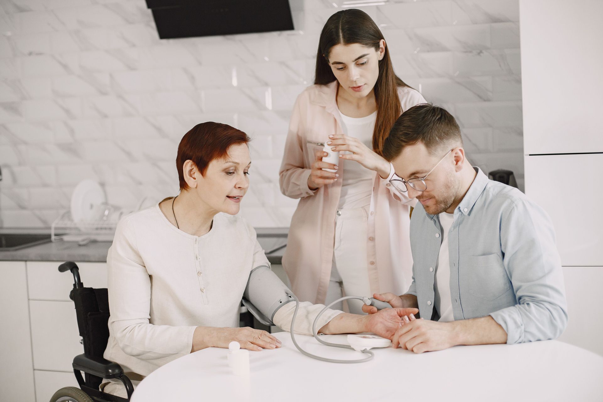 Three people gathered around a white table in a bright kitchen, examining a baby in the center.