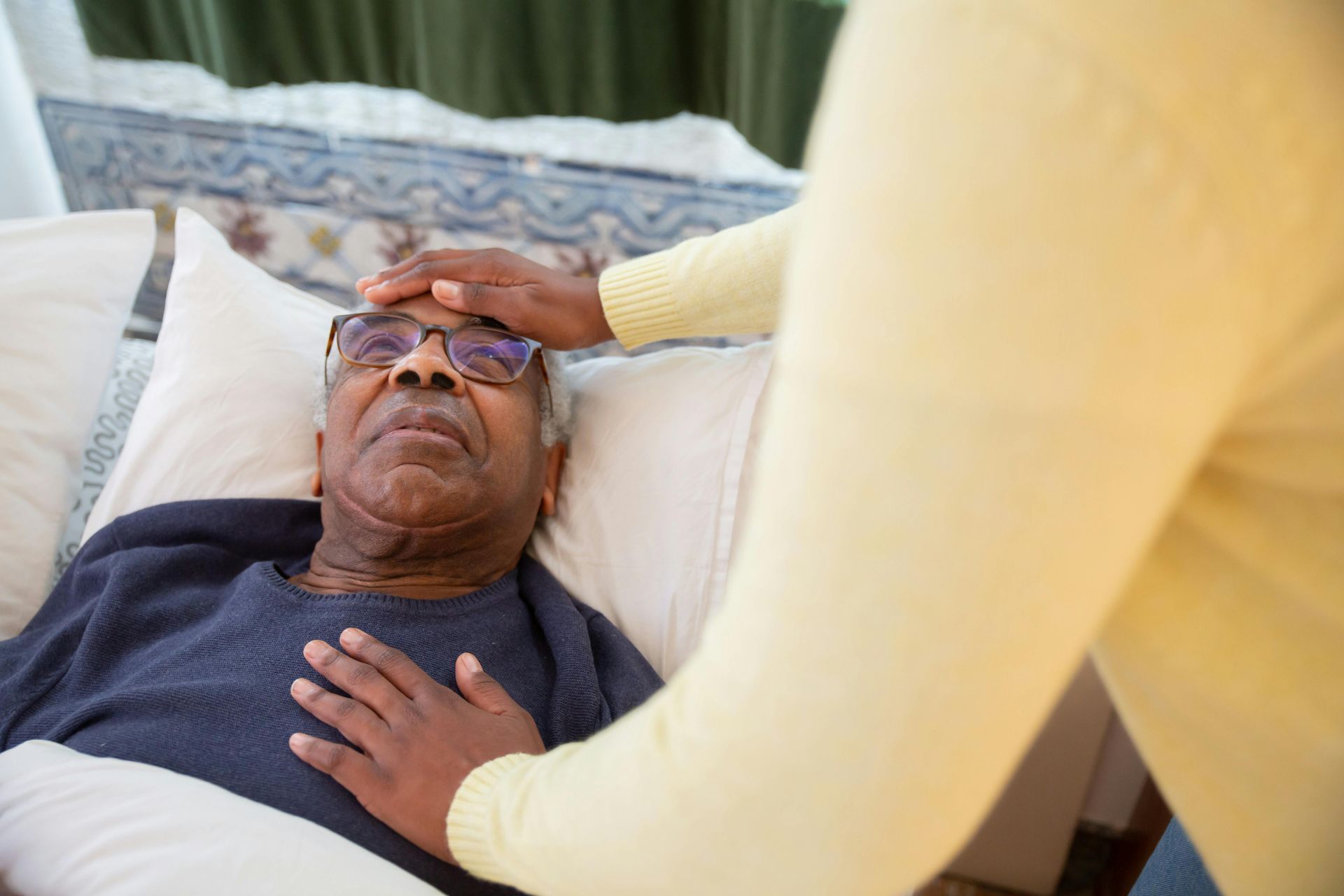 Person in bed has forehead and chest touched by another person's hands.