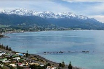 Coastal town with snow-capped mountains in the background, next to a tranquil bay.