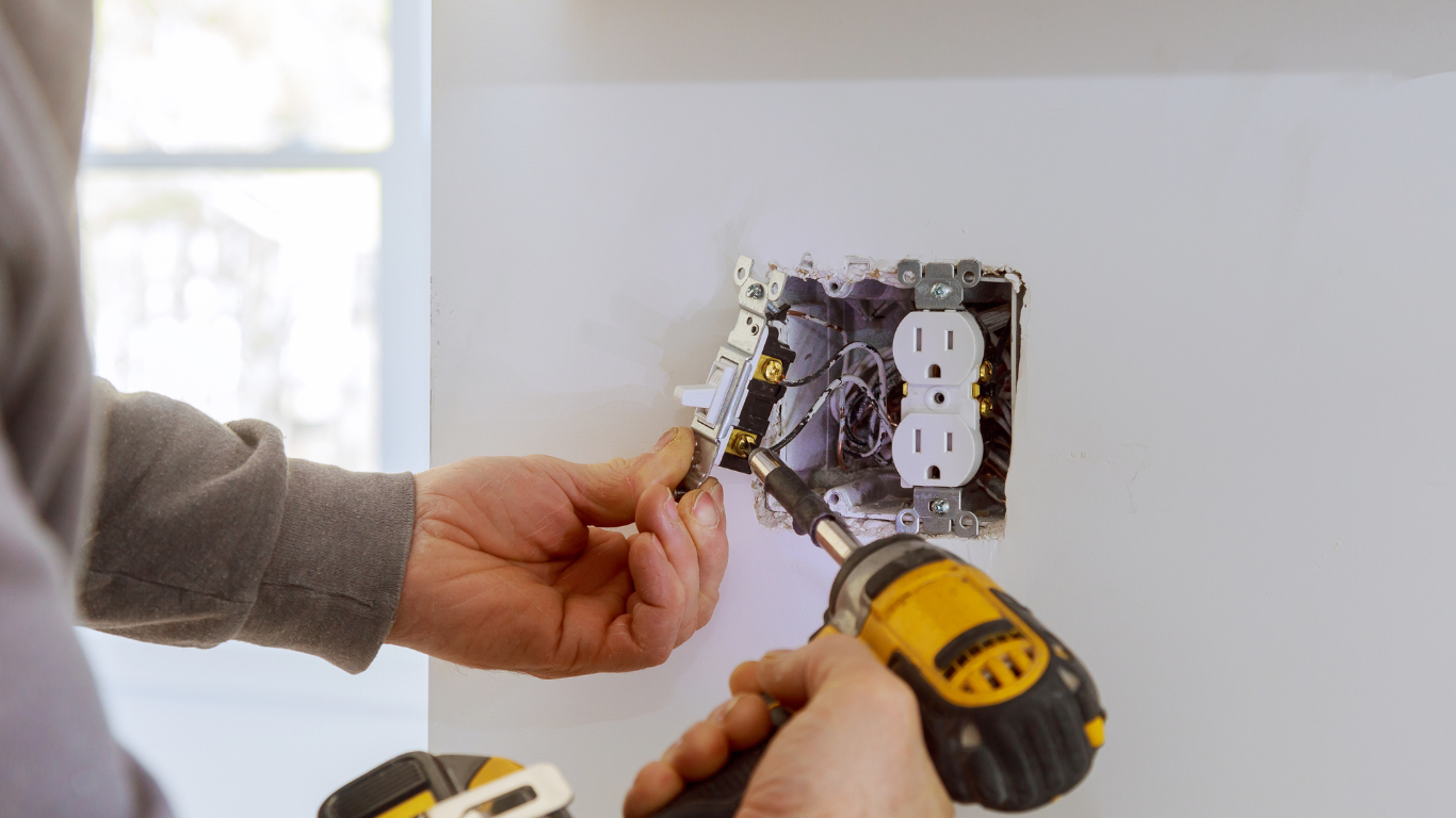 A man is installing an electrical outlet on a wall with a drill.