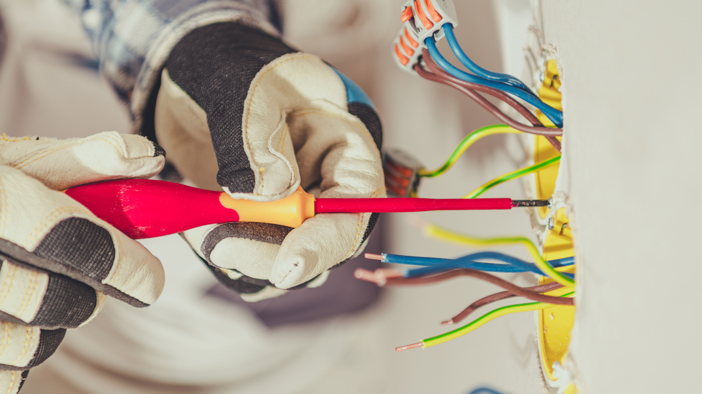 An electrician is working on a wall with a screwdriver.