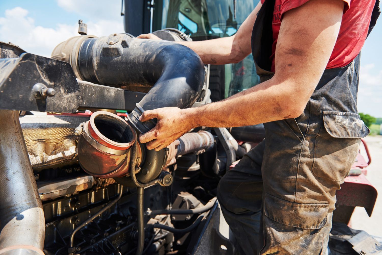Worker cleaning muddy machinery with a hose outdoors at a construction site