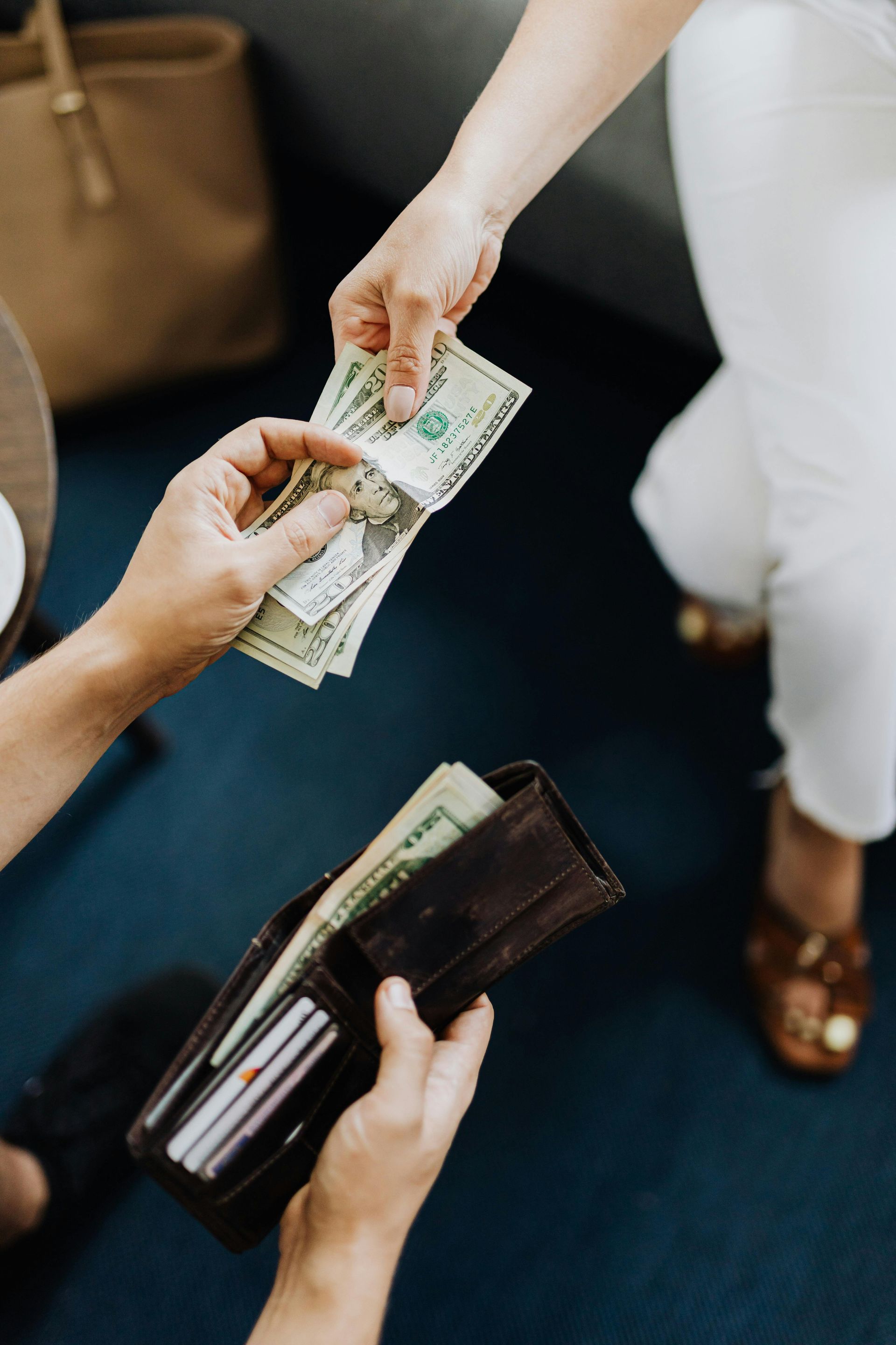 A person hands cash to another holding an open wallet on a dark floor.