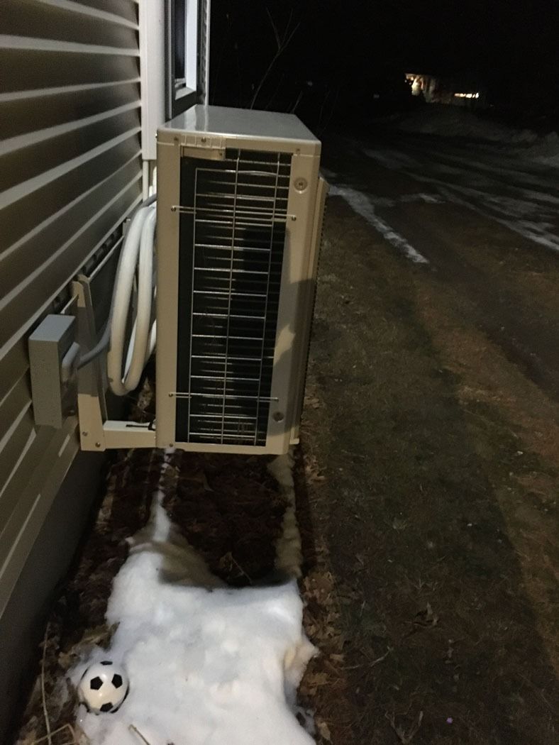 Outdoor air conditioner unit beside a house, with snow on the ground and a small soccer ball nearby.