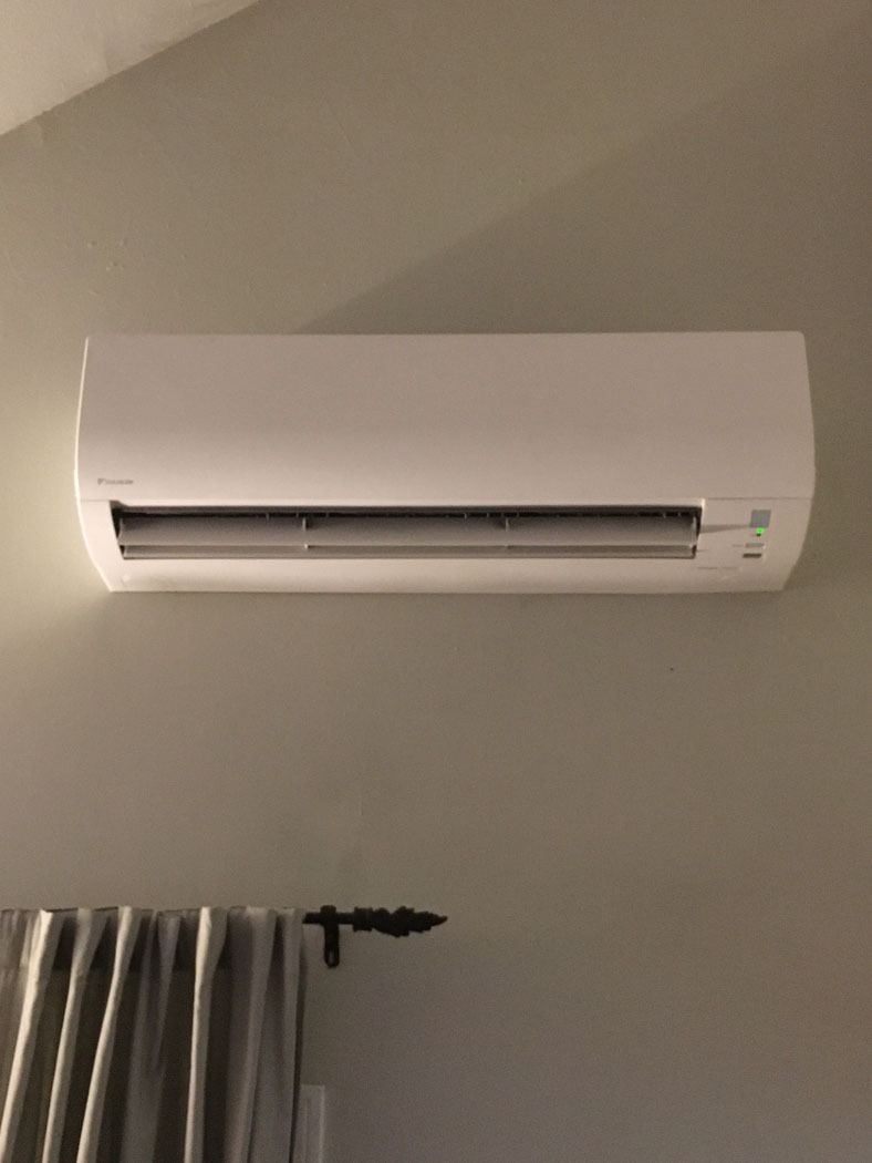 Wall-mounted white air conditioner above a gray curtain on a beige wall