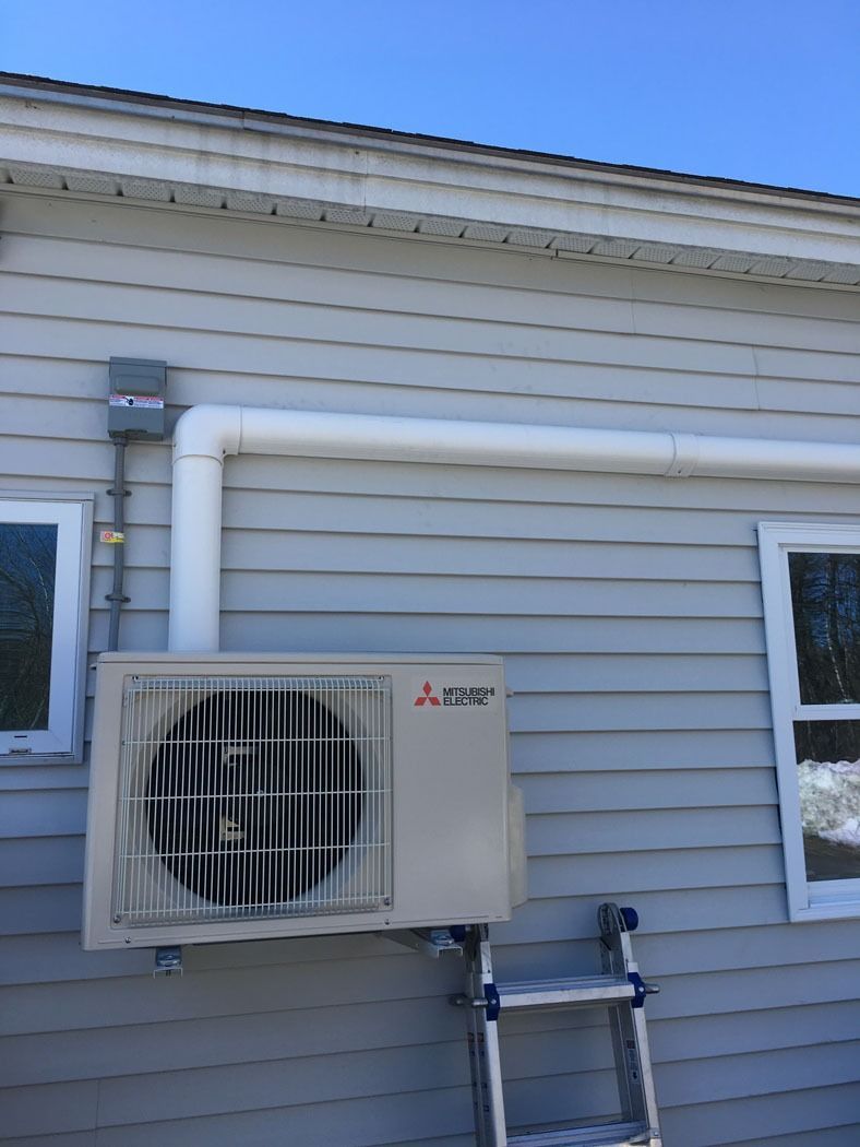 Wall-mounted outdoor air conditioner unit beside two windows on a beige house exterior