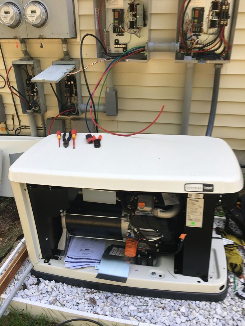 White portable generator with open side panel in front of electrical utility equipment outdoors.