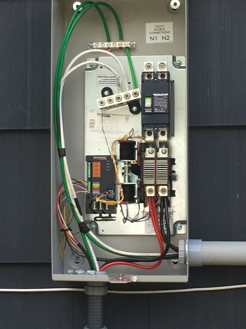 Open electrical breaker panel with wiring, switches, and green cables in a metal box.