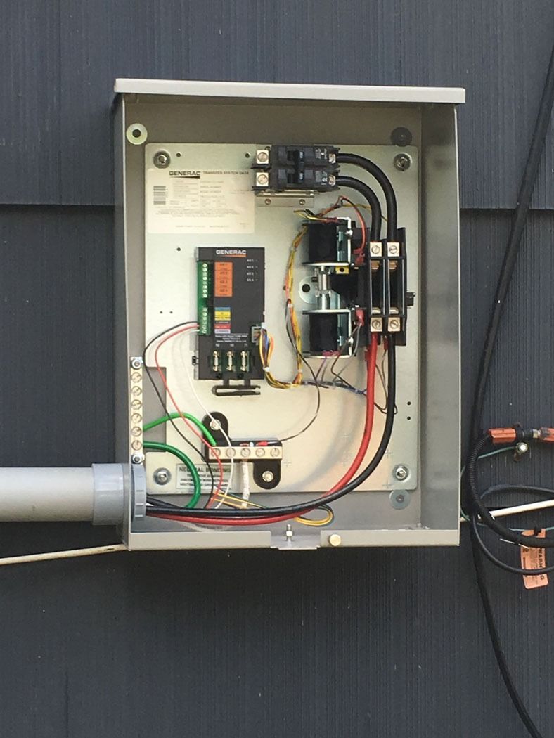 Open electrical control panel mounted on a dark exterior wall with visible wiring and components